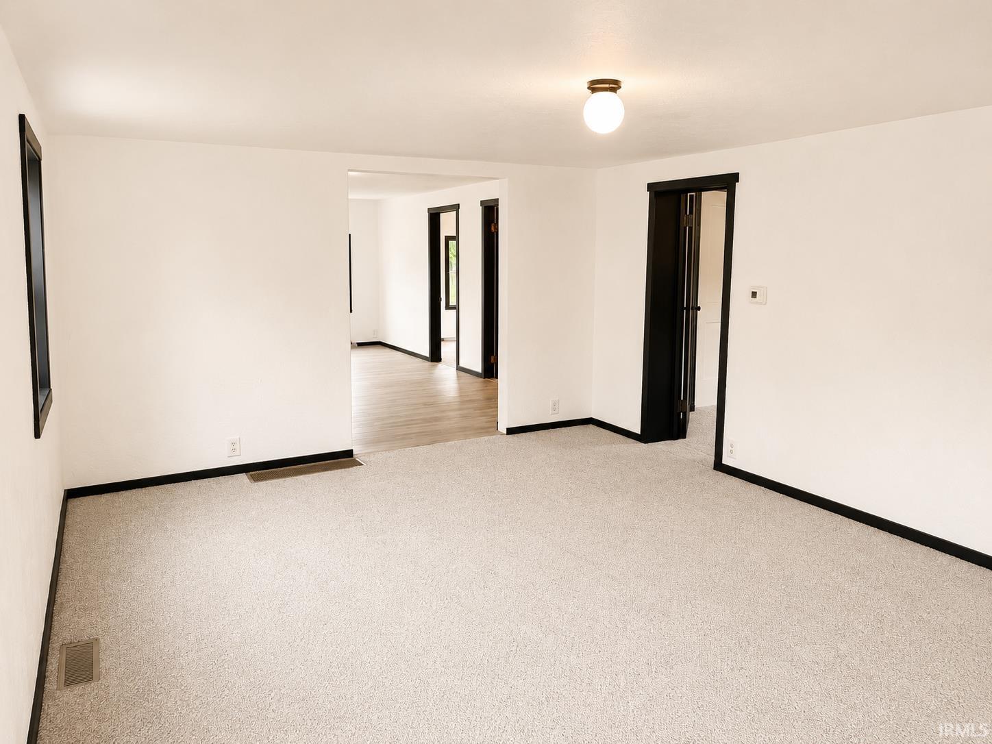 Spacious room featuring light-toned carpeting and white walls with contrasting dark trim