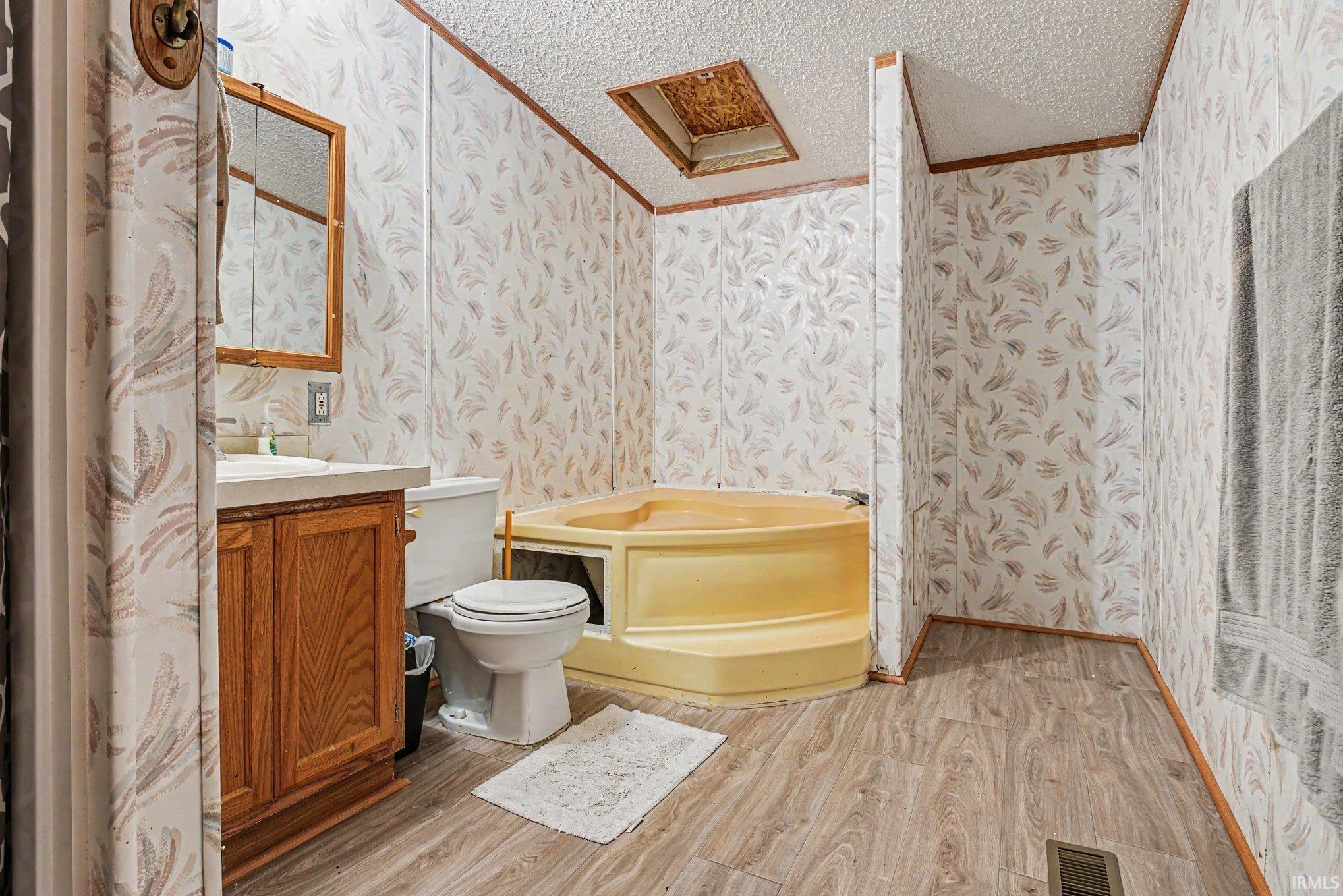 Bathroom featuring a corner soaking tub, wood-finish flooring, a vanity with a wood cabinet, and a wall-mounted medicine cabinet