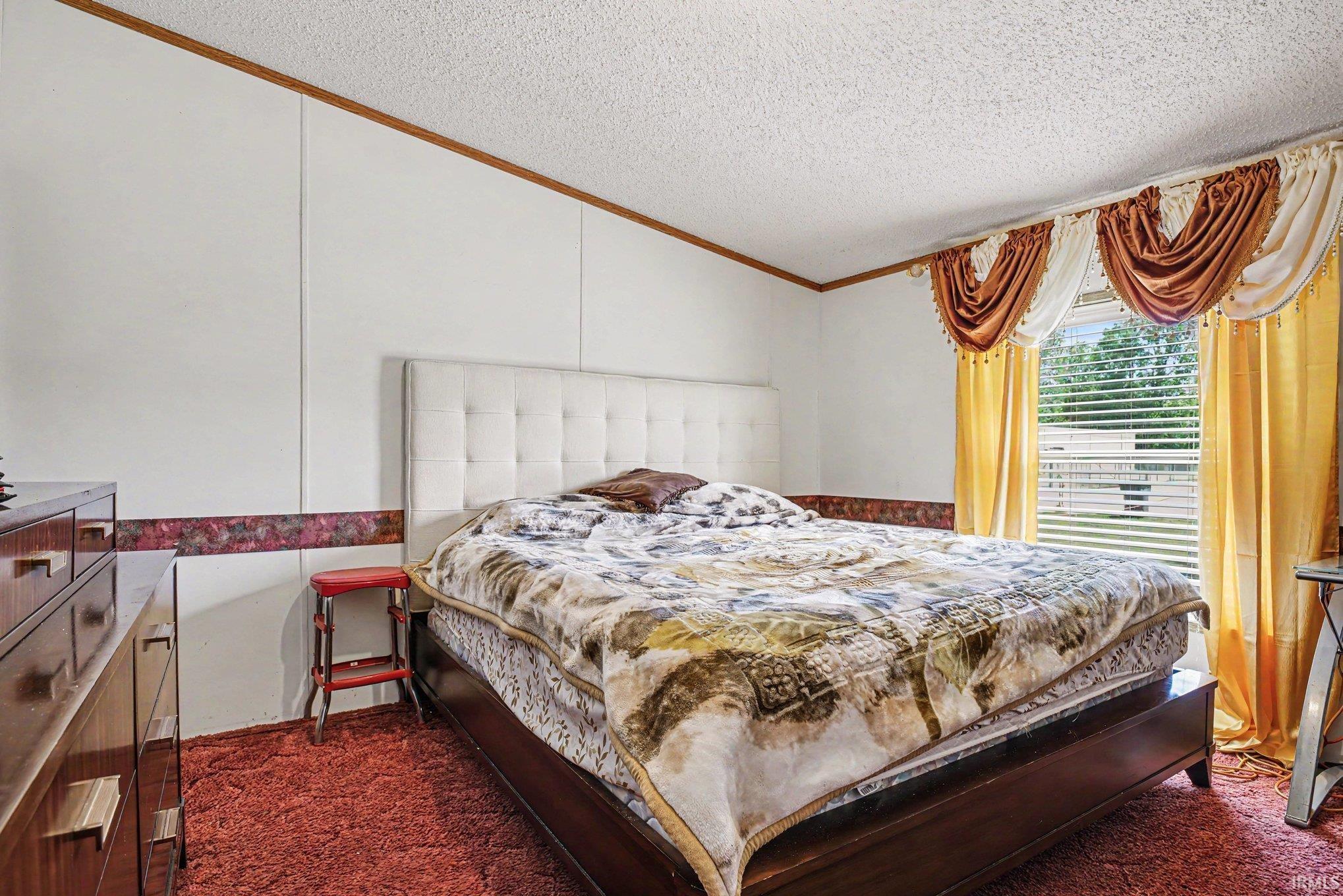 Spacious bedroom featuring white panel walls, wood trim, and textured ceiling