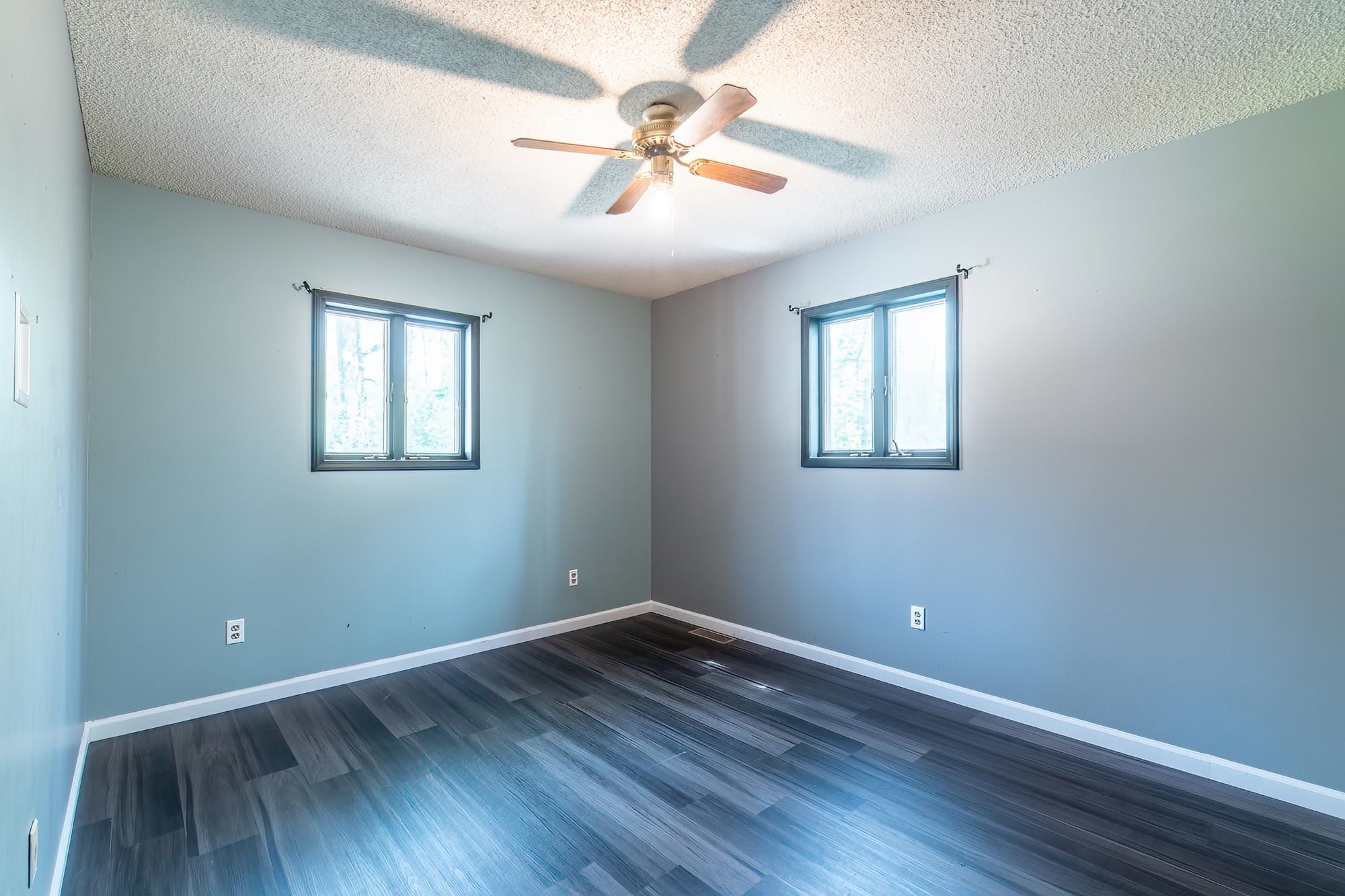 Interior room featuring two paneled windows, a ceiling fan with light fixture, and wood-finish flooring