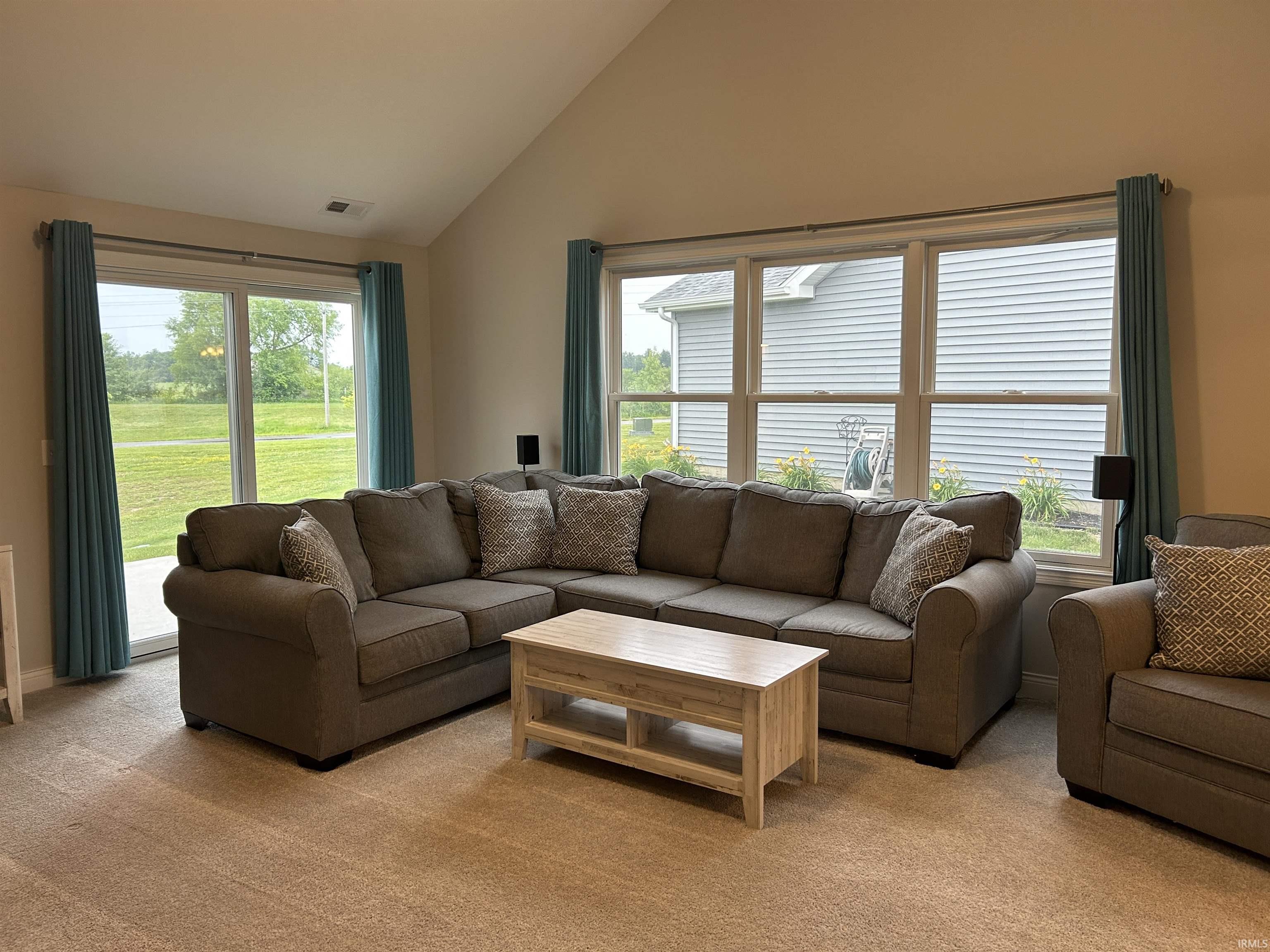 Vaulted ceiling living space featuring multiple windows, a sliding glass door, and carpet flooring