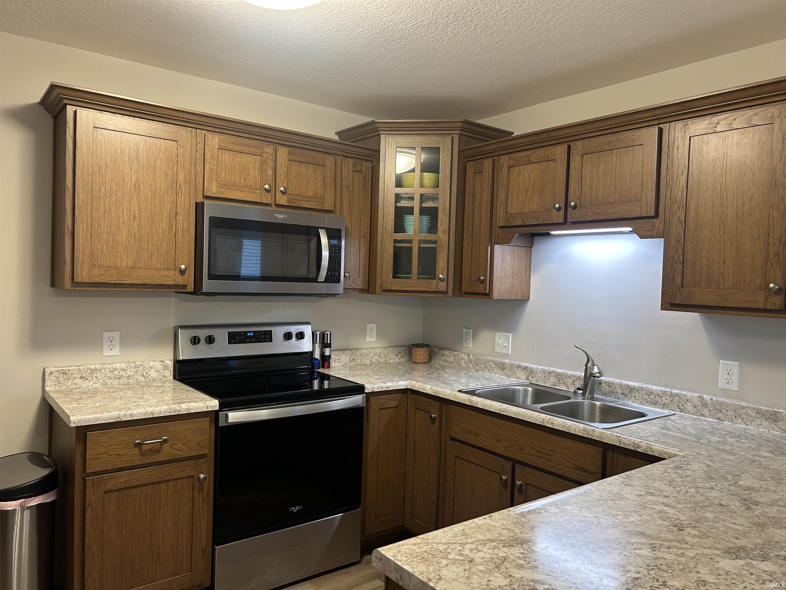 U-shaped kitchen featuring wood cabinetry, light-toned countertops, and stainless steel appliances including an oven range and over-the-range microwave
