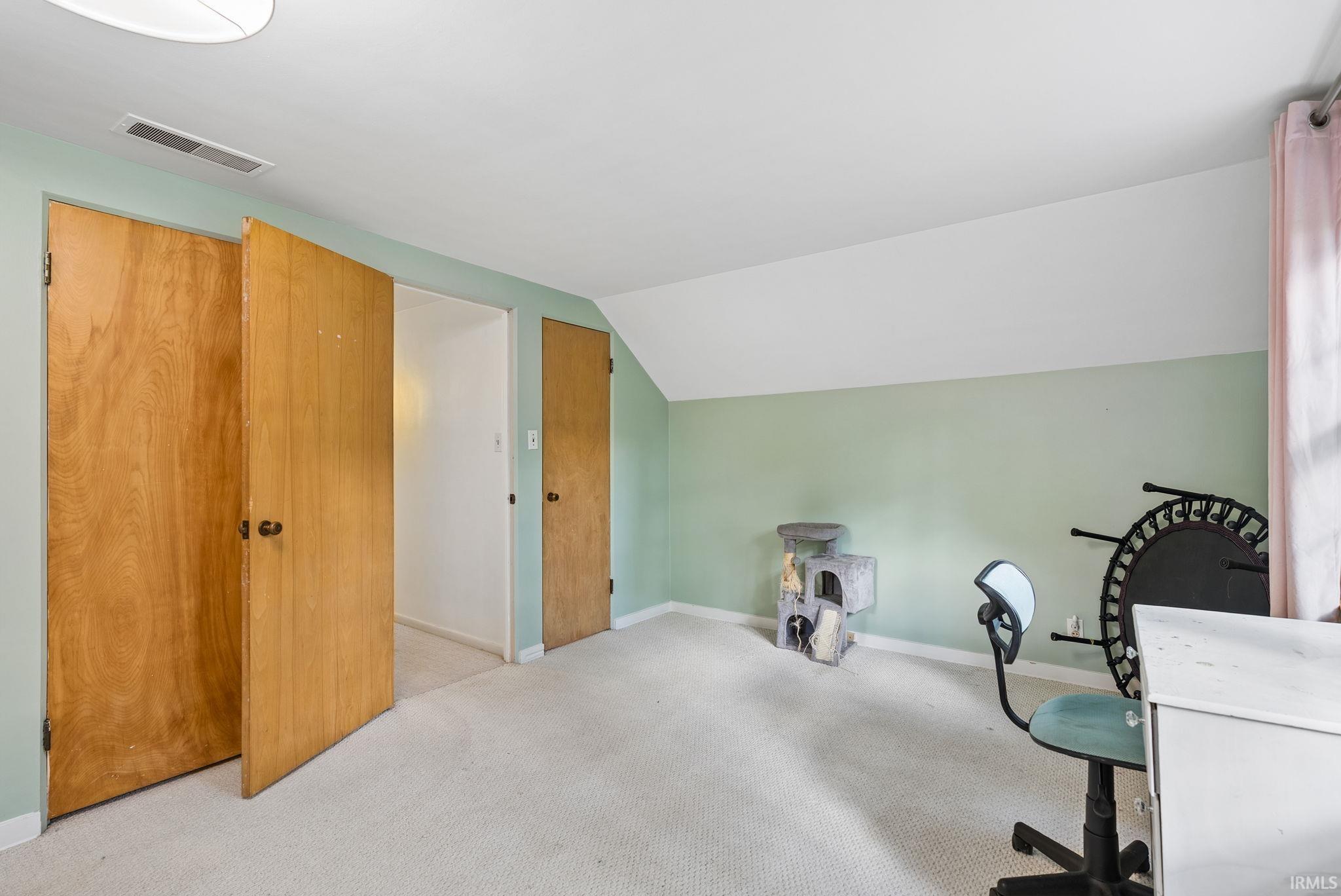 Carpeted room featuring light green walls, a sloped ceiling, and multiple wood-panel doors