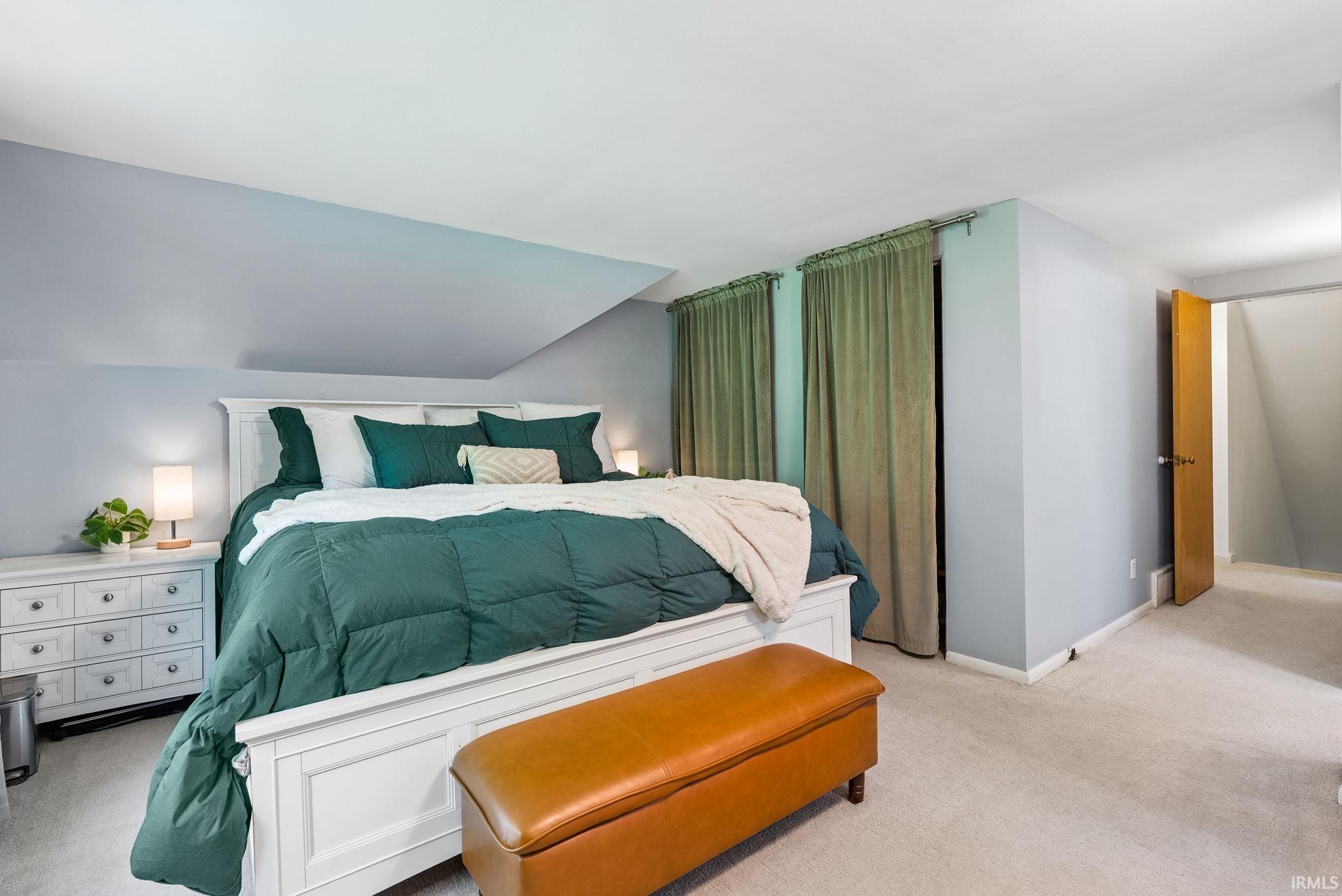 Carpeted room featuring a sloped ceiling, light blue walls, and a light wood-finish door frame
