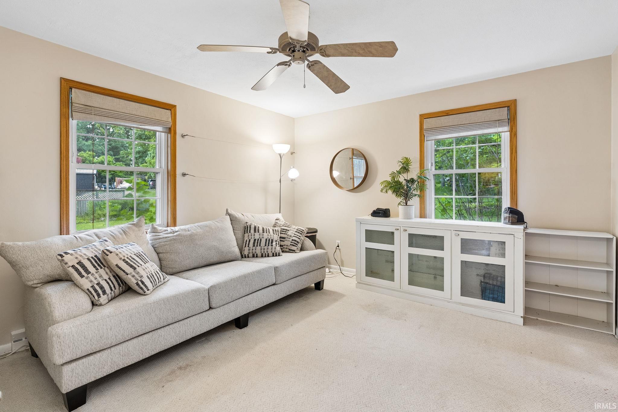 Bright room featuring a ceiling fan, two large windows with wood-finish trim, and light-toned carpet flooring