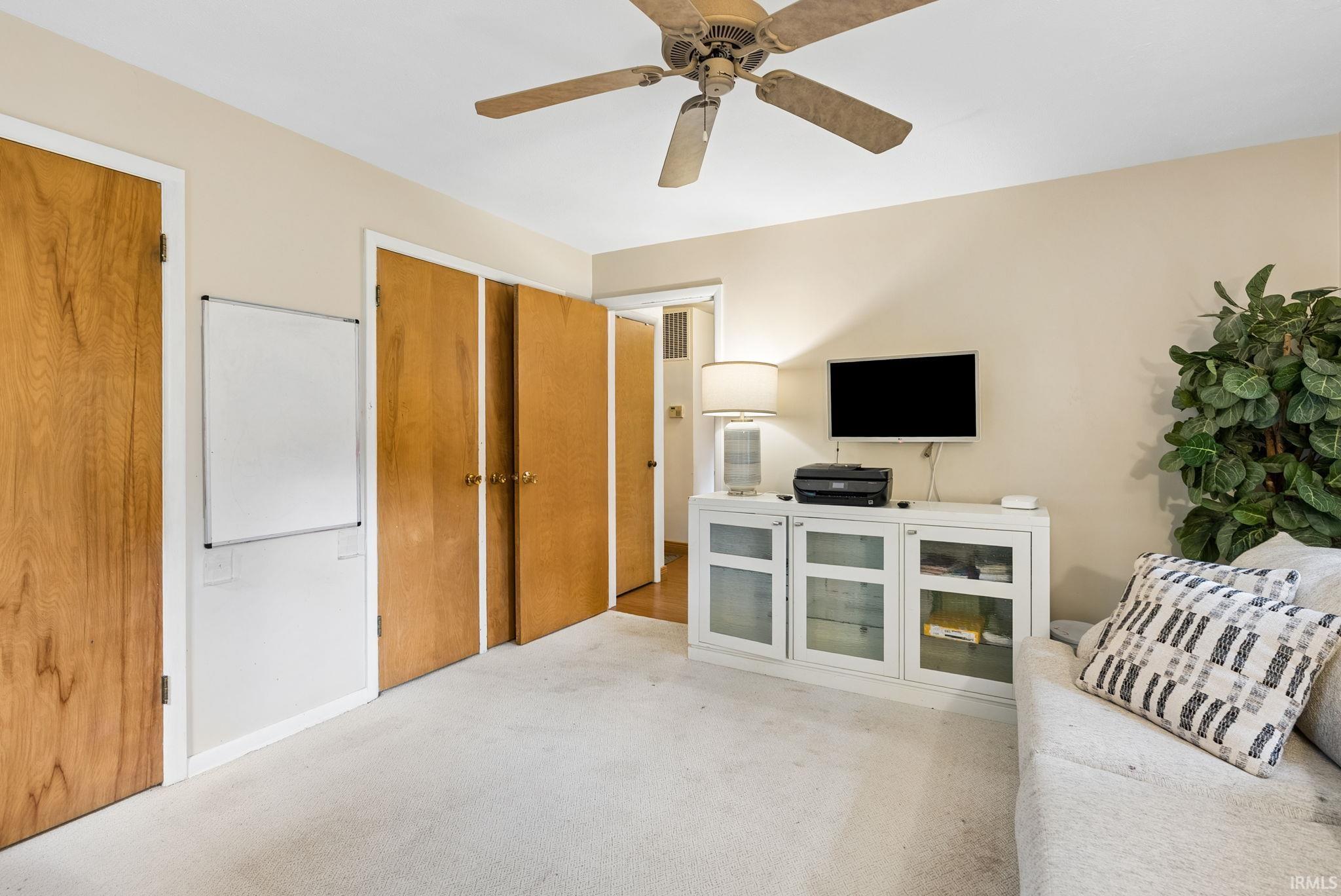Carpeted room featuring a ceiling fan, light-toned walls, and multiple wood-paneled doors