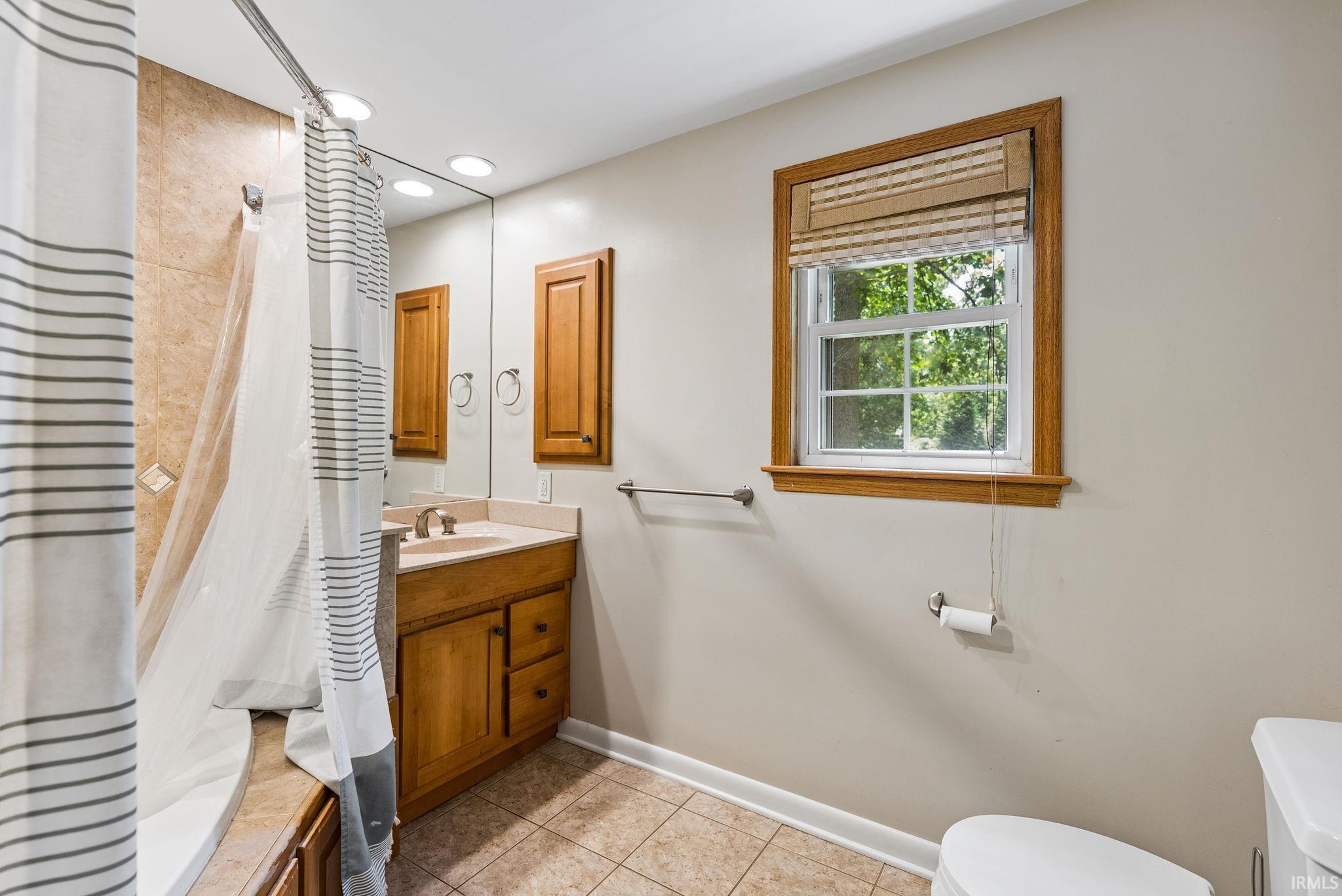 Bathroom featuring a vanity with a light wood-finish cabinet and a light-toned countertop, a large wall-mounted mirror, and tile flooring