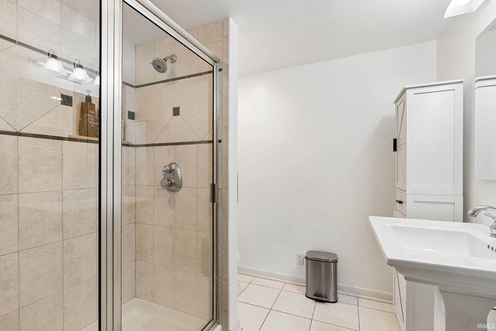 Glass-enclosed shower with tile surround and integrated shelving, complemented by a pedestal sink and chrome fixtures