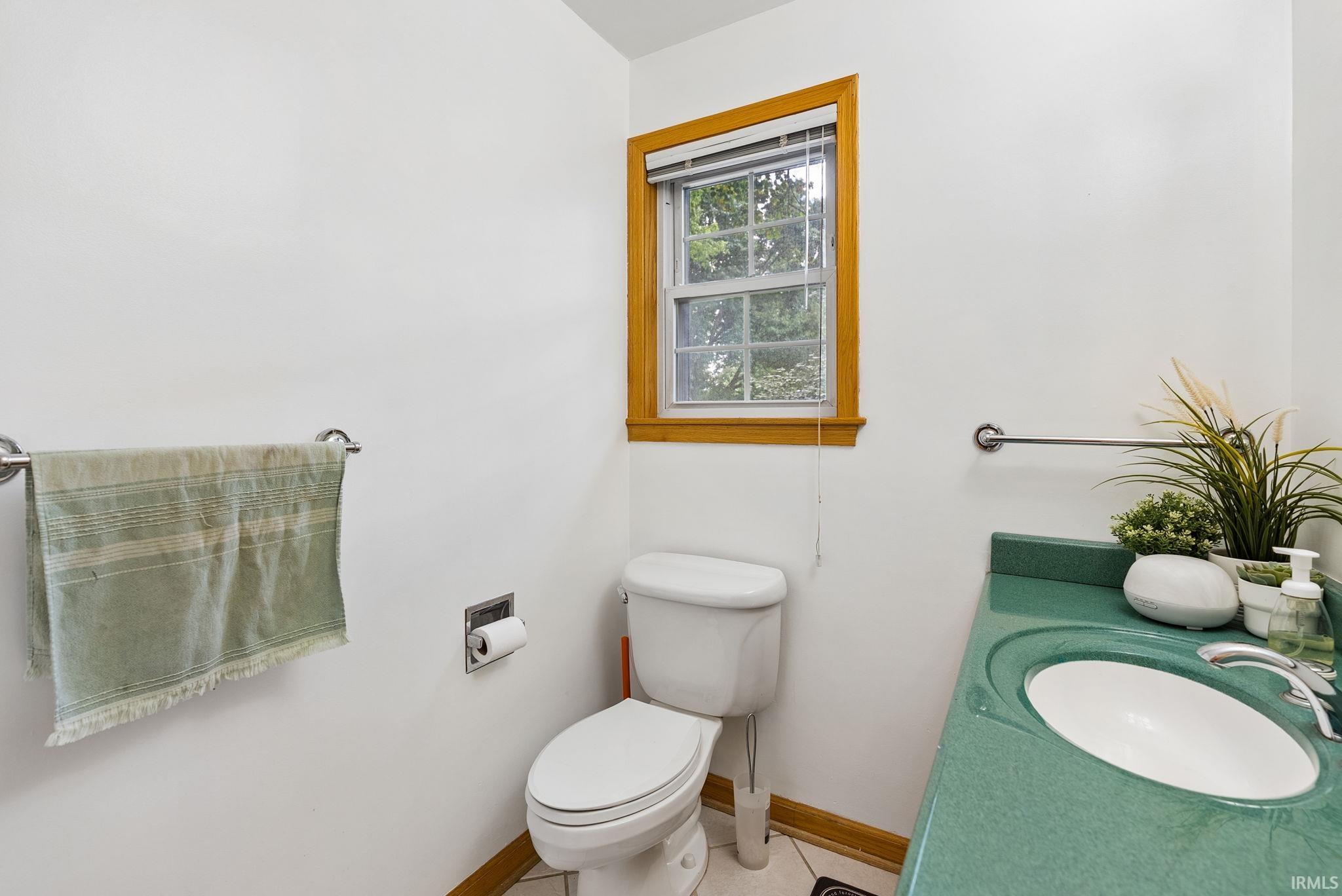 Bathroom featuring a window with wood trim, a white toilet, and a green countertop with an integrated sink