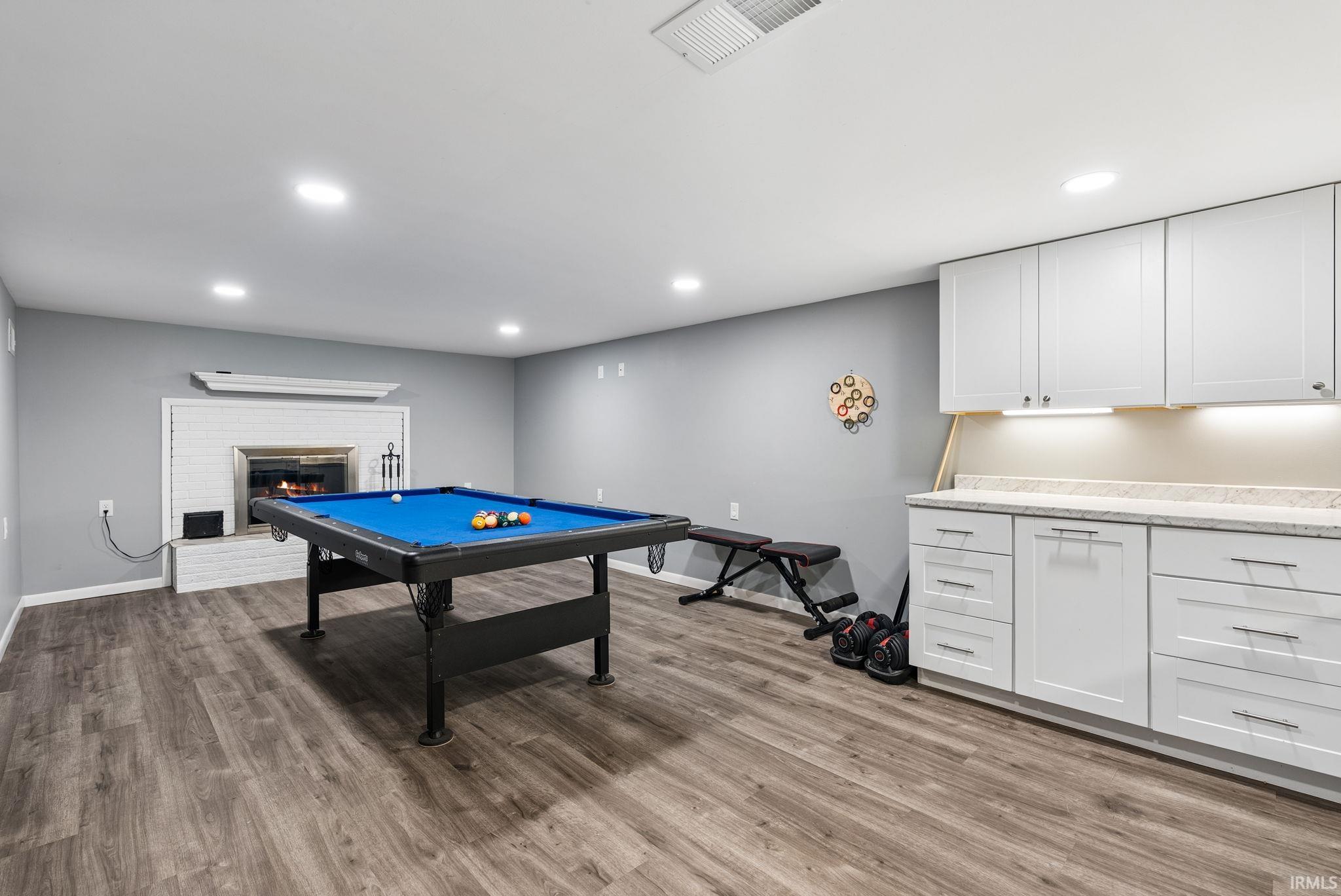 Spacious room featuring wood-finish flooring, recessed lighting, and a white brick fireplace