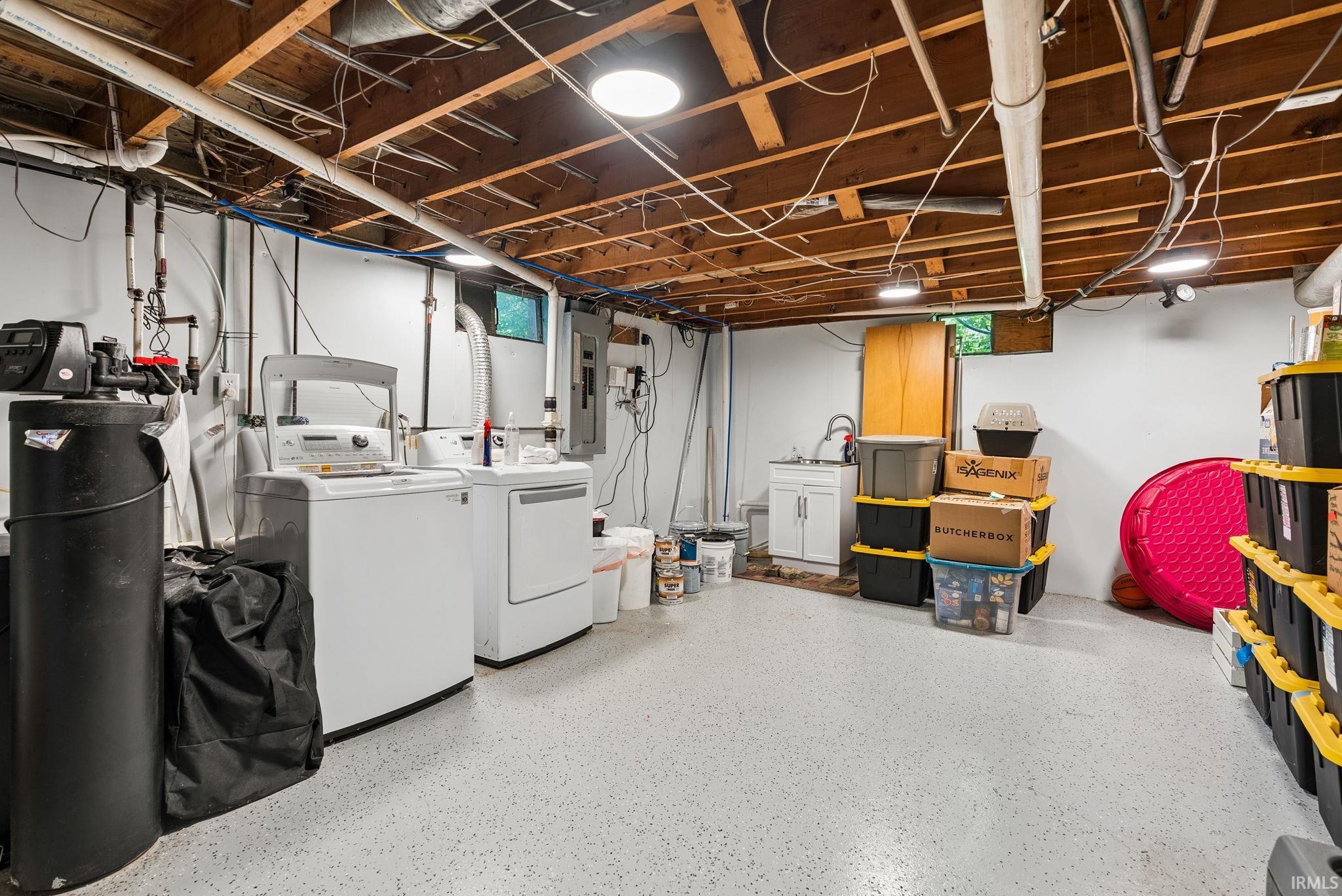 Finished basement space featuring exposed wood joists, utility sink, white washer and dryer, and overhead lighting