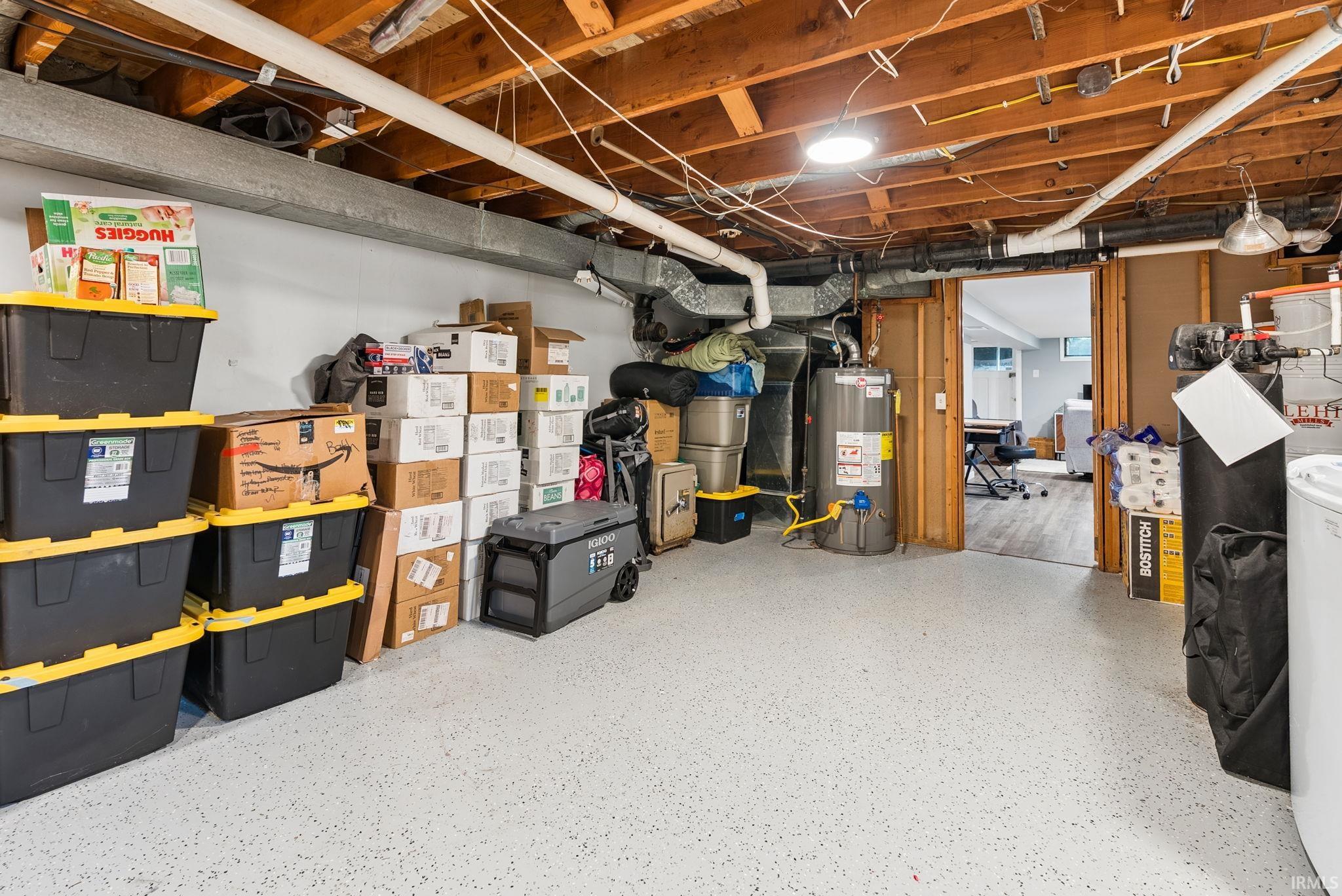 Utility space featuring exposed ceiling joists, overhead lighting, a water heater, visible ductwork, and a partial view of an adjacent finished room