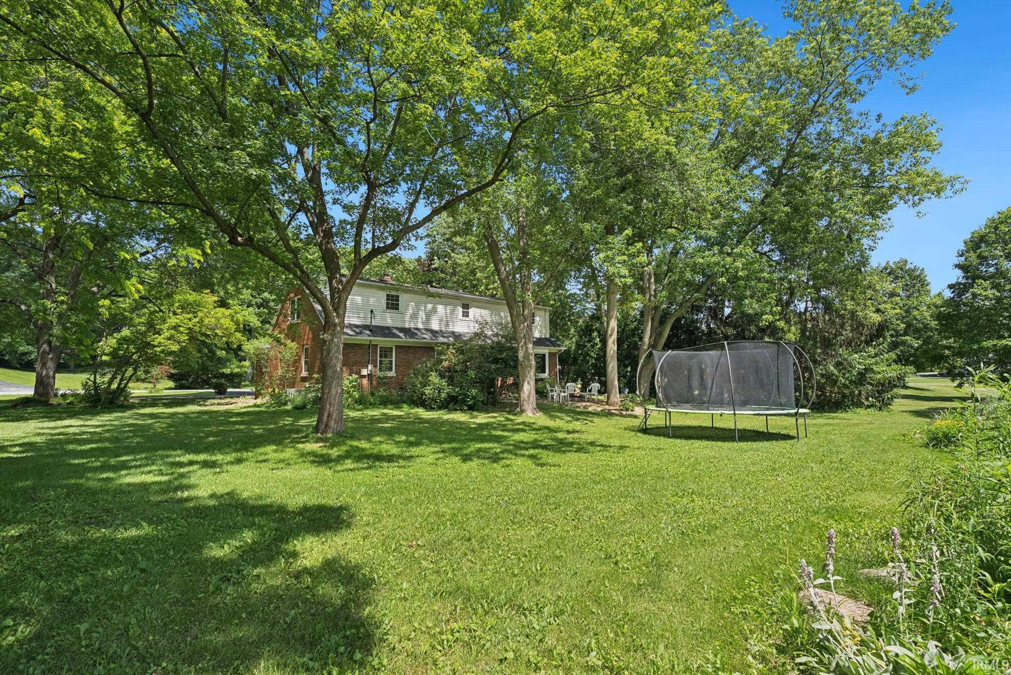 Expansive green lawn with mature shade trees surrounding a two-story residence featuring brick and white siding