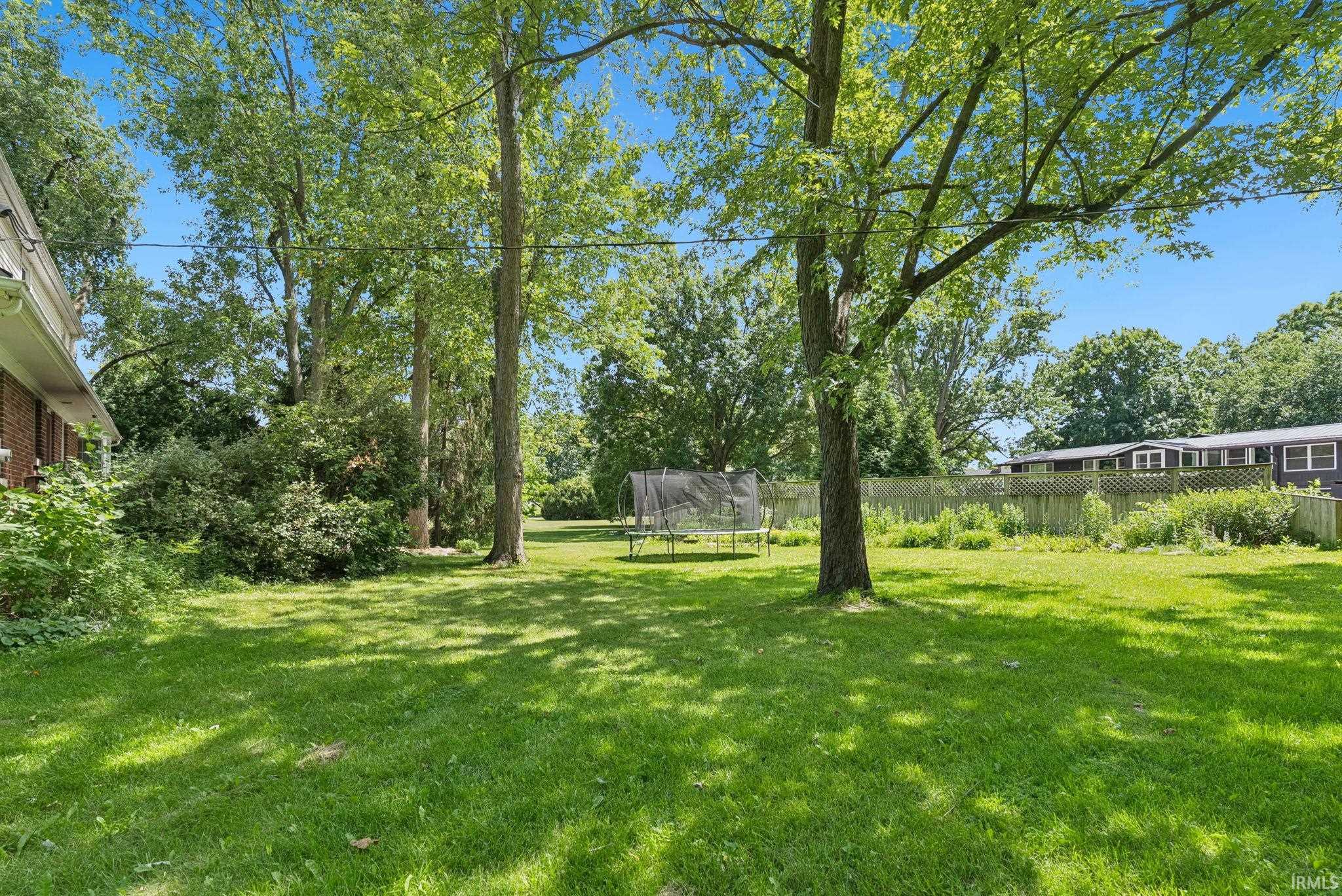 Expansive grassy yard featuring mature trees and established perimeter landscaping