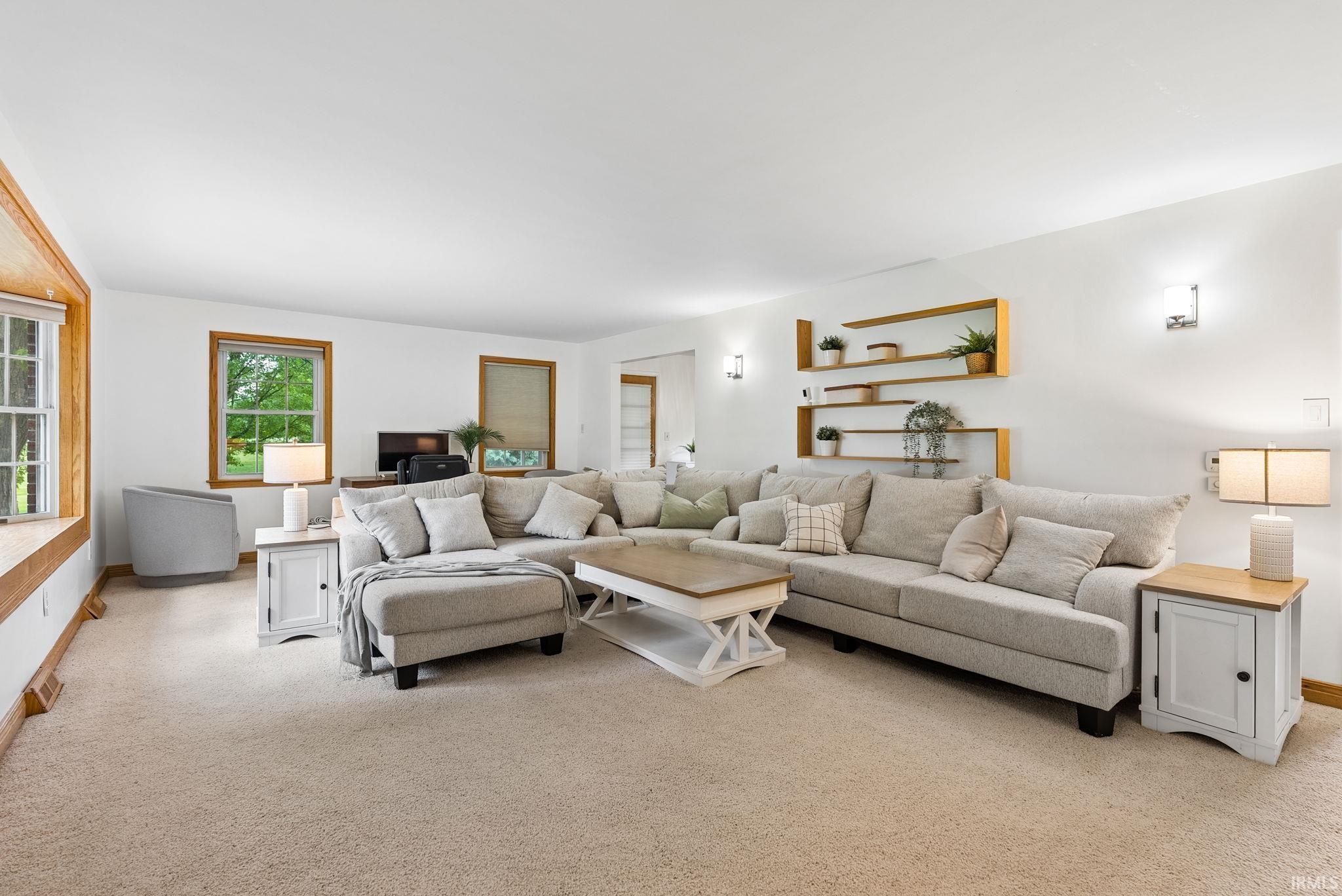 Carpeted living area featuring multiple windows with wood trim, built-in shelving, and wall-mounted sconces