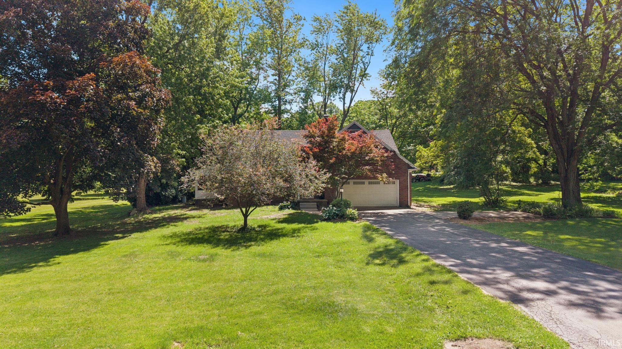 Brick exterior featuring an attached two-car garage, asphalt driveway, and mature landscaping
