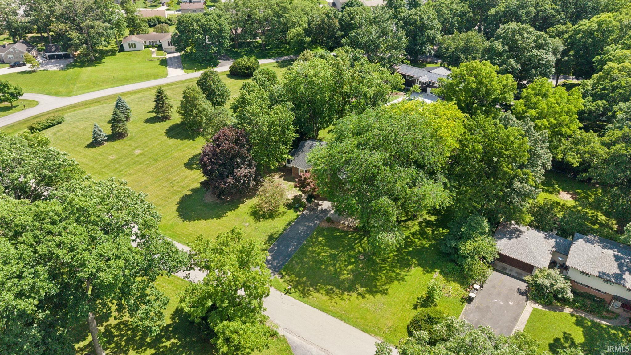 Expansive property featuring mature trees, a broad green lawn, and a paved driveway
