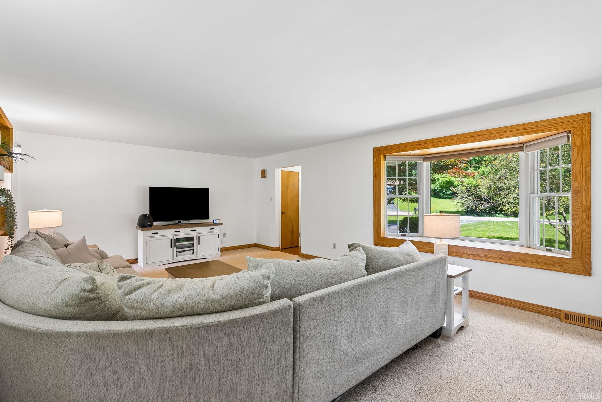 Living area featuring a prominent bay window with wood trim, white walls, and carpet flooring