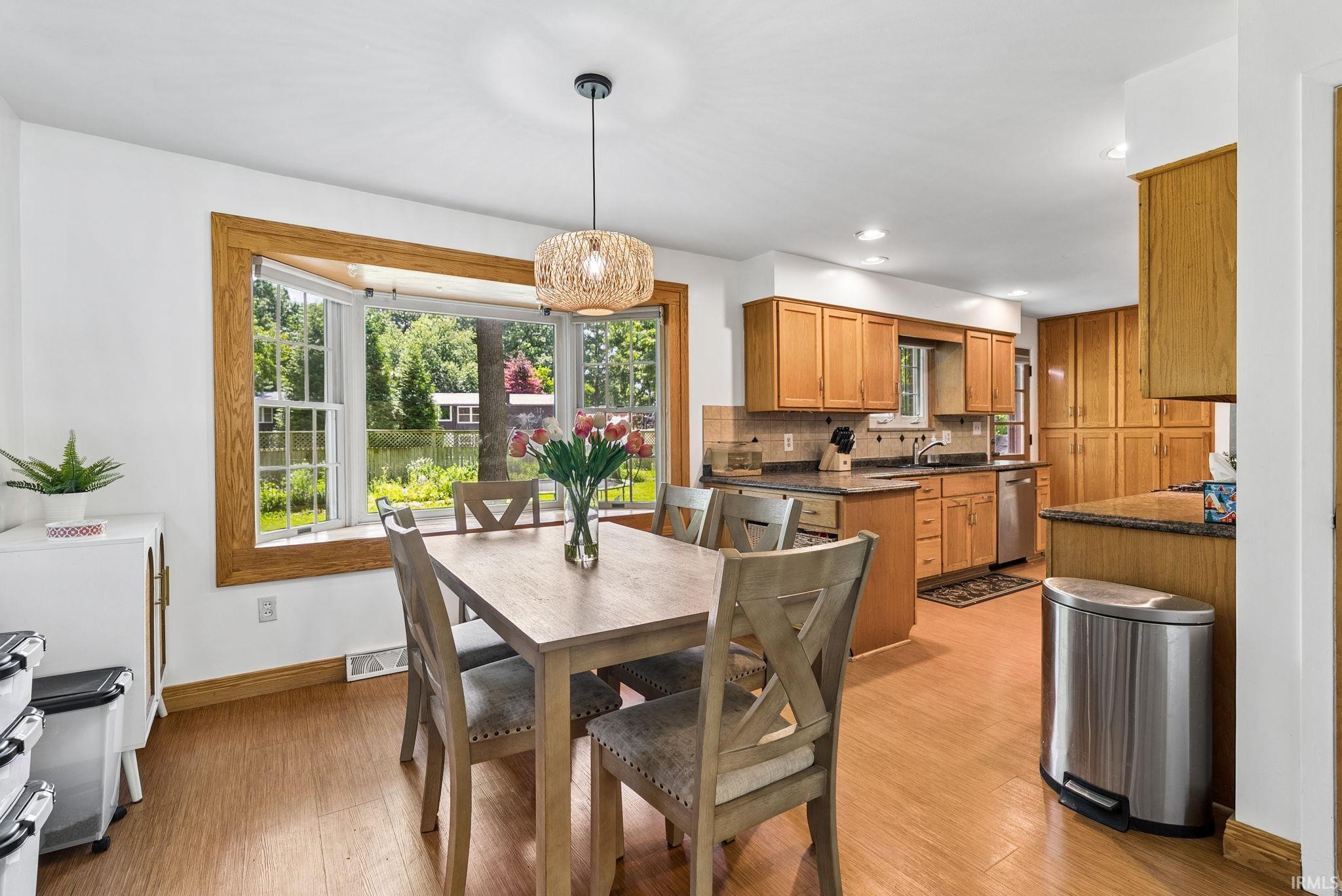 Eat-in kitchen featuring wood-finish flooring, a bay window with wood trim, ample wood cabinetry, and a tile backsplash