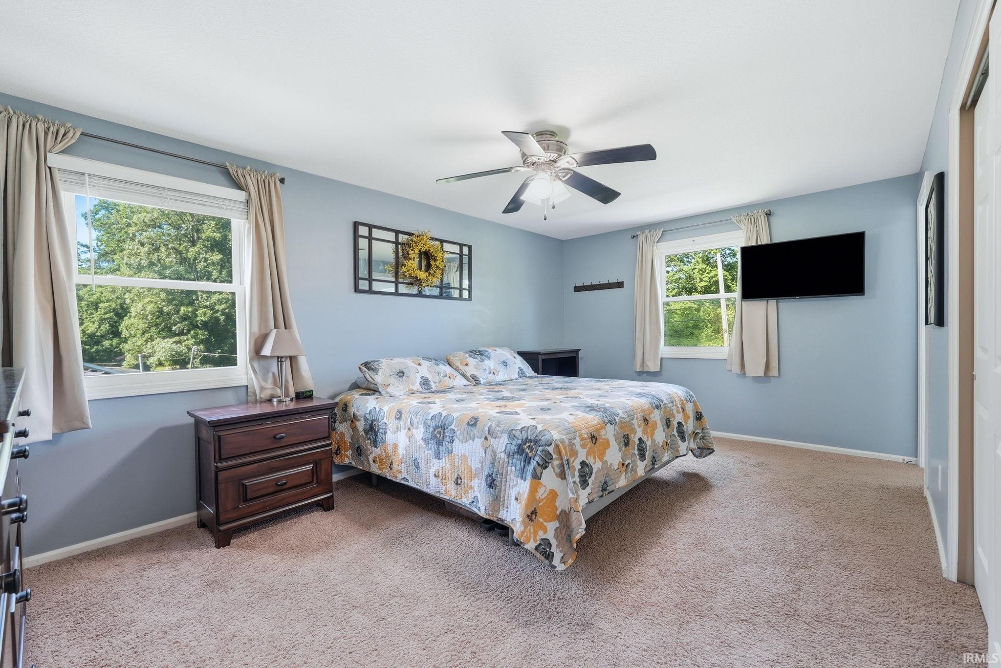 Spacious room featuring light blue walls, two windows with window treatments, a ceiling fan with integrated lighting, and carpet flooring