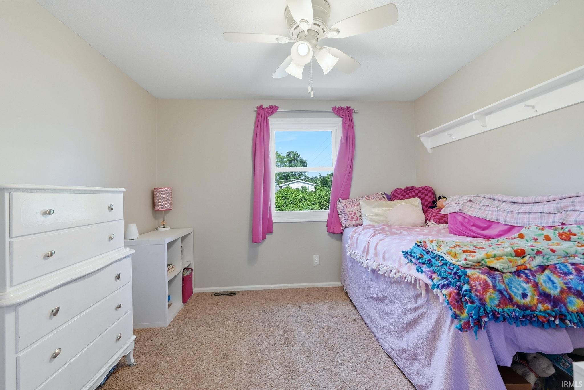 Carpeted room featuring a white window frame, a built-in wall shelf, light-colored walls, and a ceiling fan with integrated lighting
