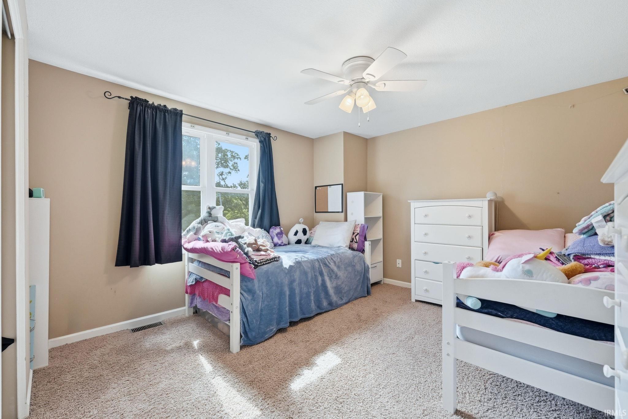 Carpeted room featuring a ceiling fan with integrated lighting, a window with dark curtains, and light-toned walls