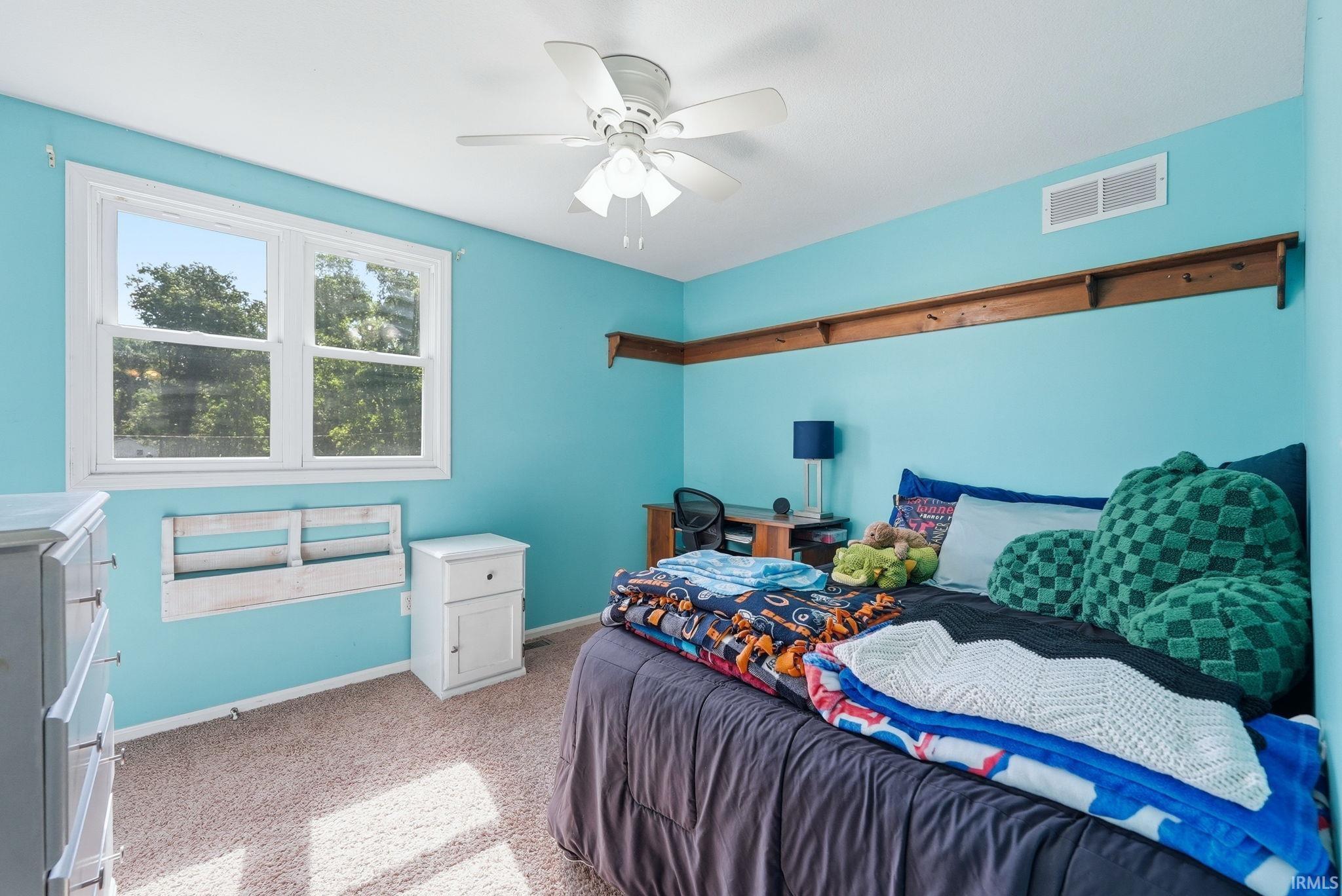 Bright bedroom with a double window, wood-finish shelving, and a ceiling fan