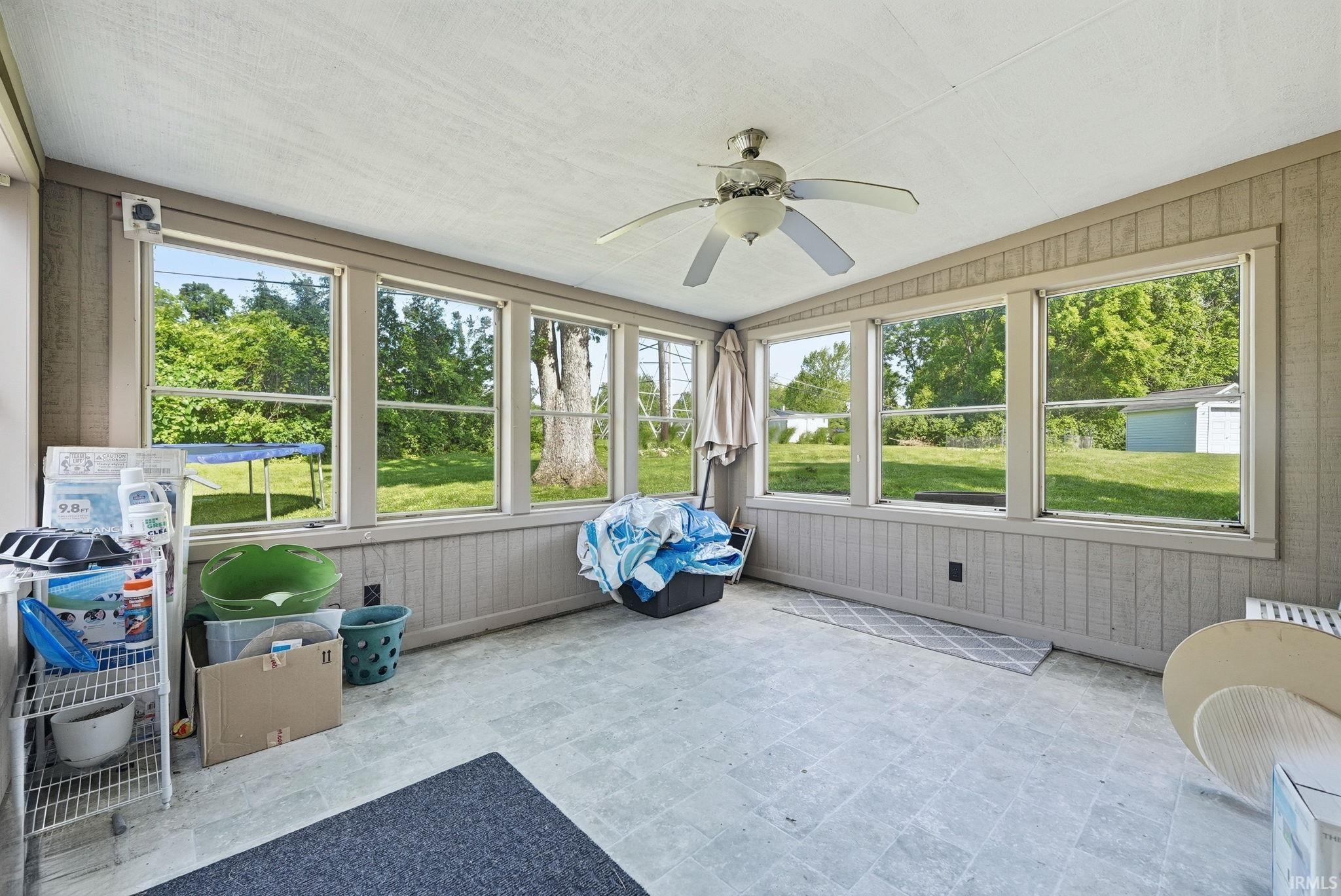 Sunroom featuring extensive window-lined walls, a ceiling fan fixture, paneled walls, light-toned flooring, and a flat ceiling