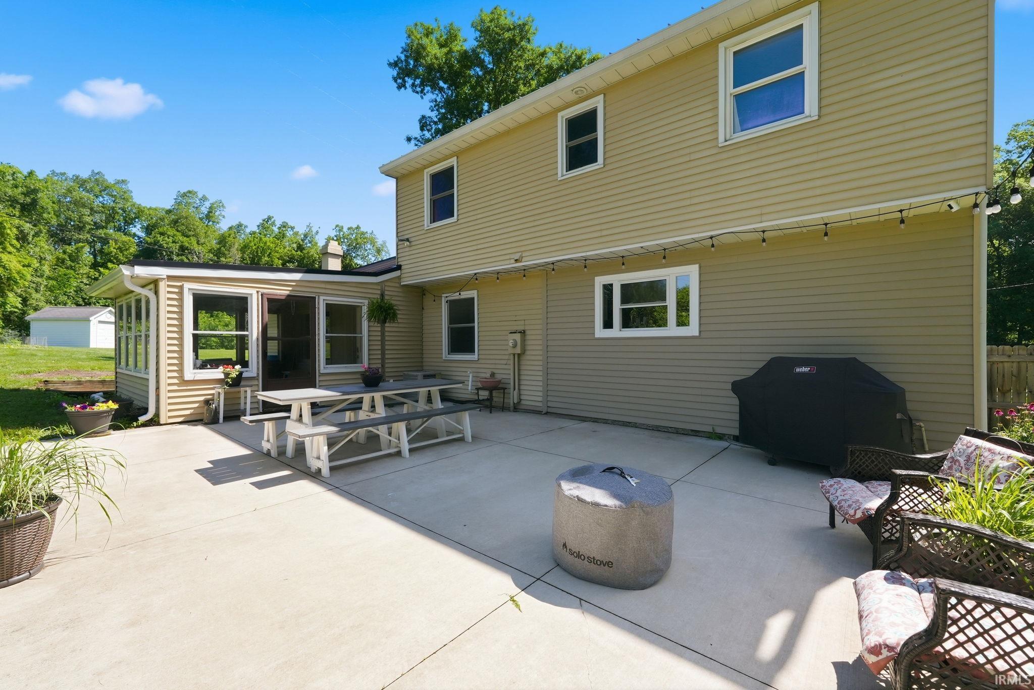 Expansive concrete patio offering direct access to an enclosed sunroom with multiple windows