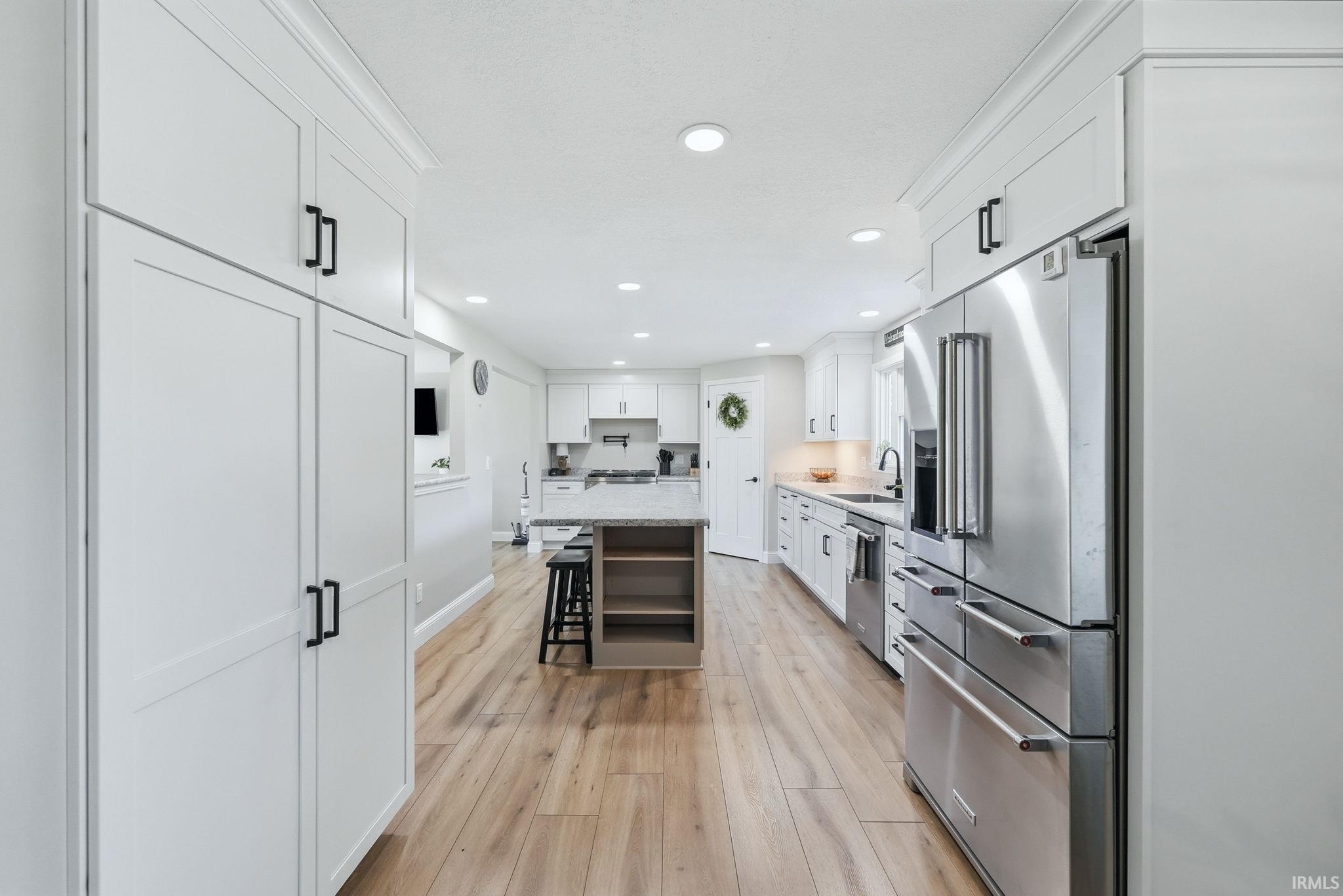 Modern kitchen featuring extensive white cabinetry, stainless steel appliances, a center island with countertop seating, recessed lighting, and wood-finish flooring