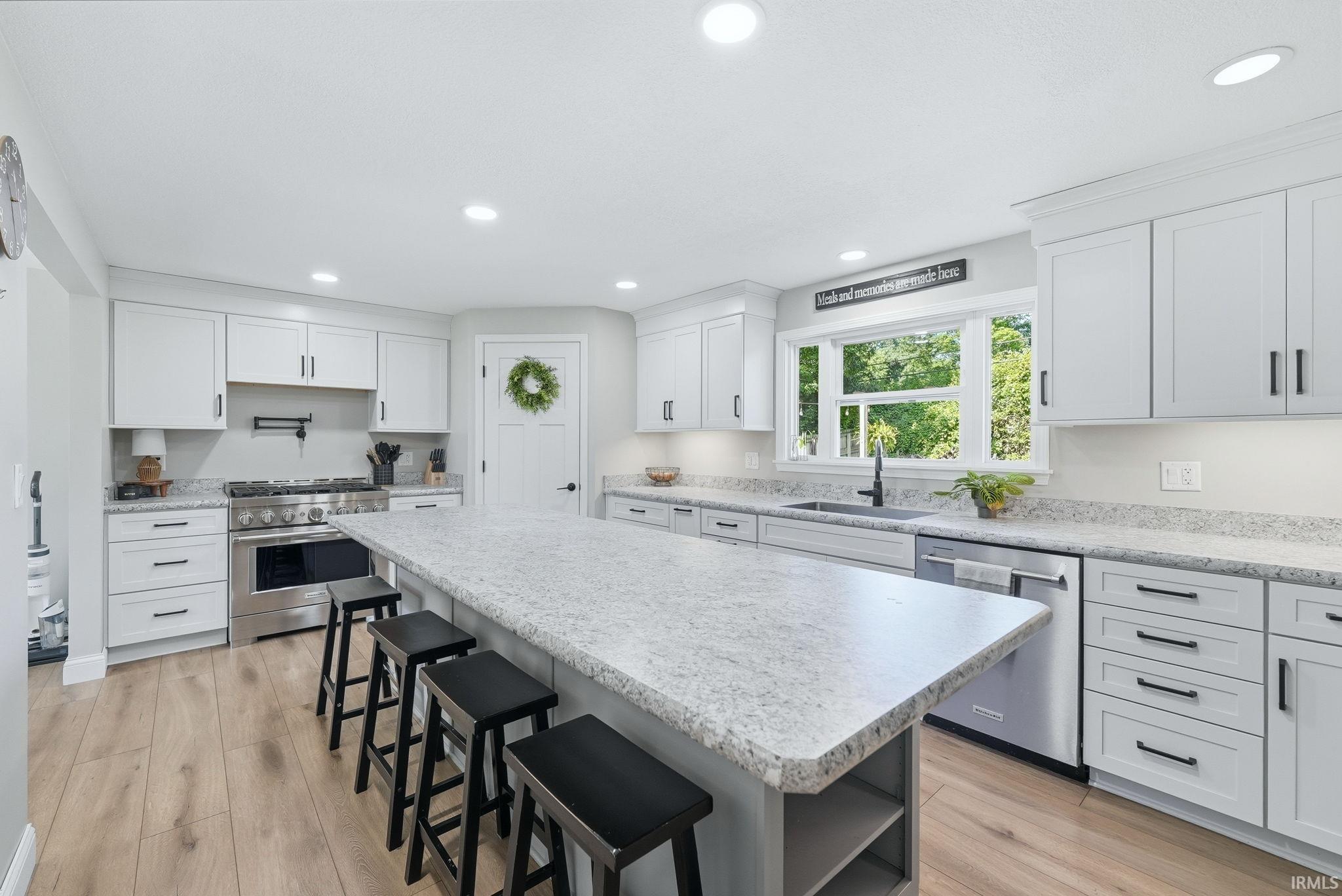 Modern kitchen featuring light-toned cabinetry with dark hardware, wood-finish flooring, a large center island with a light-toned countertop, and stainless steel appliances