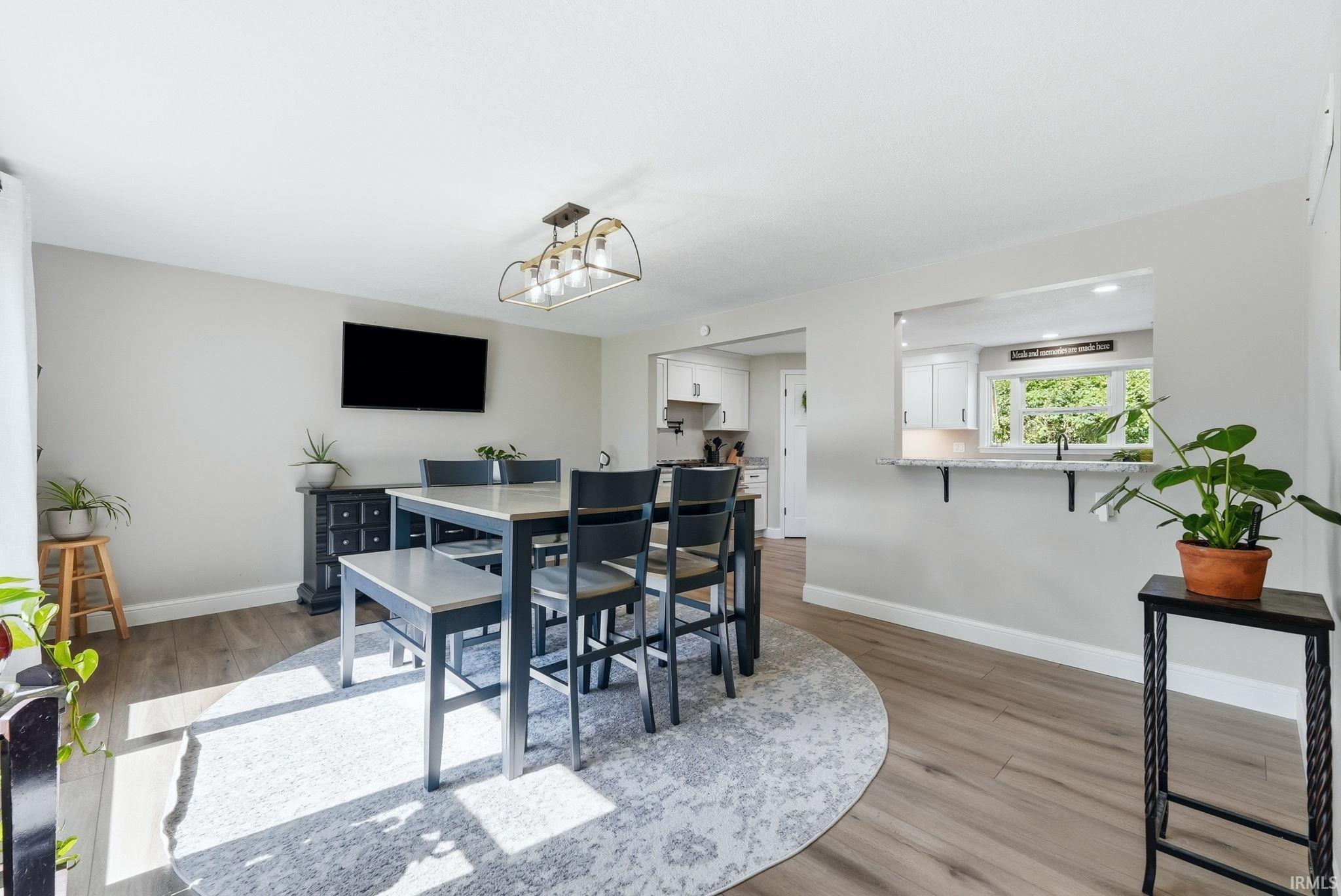 Dining area featuring wood-finish flooring, a contemporary chandelier, and a pass-through window with a stone countertop