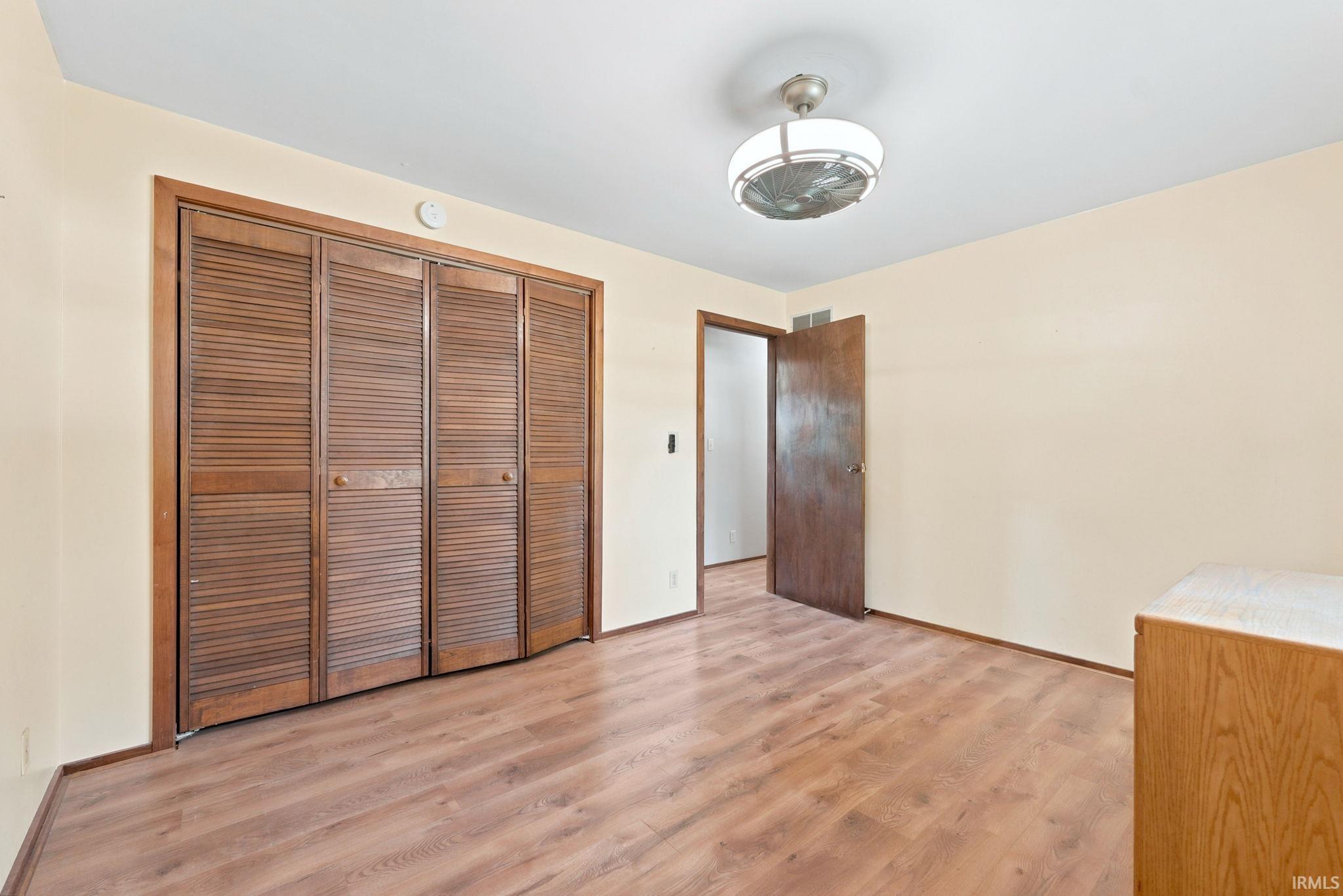 Wood-finish flooring with louvered bi-fold closet doors, a ceiling fan with integrated lighting, and painted walls