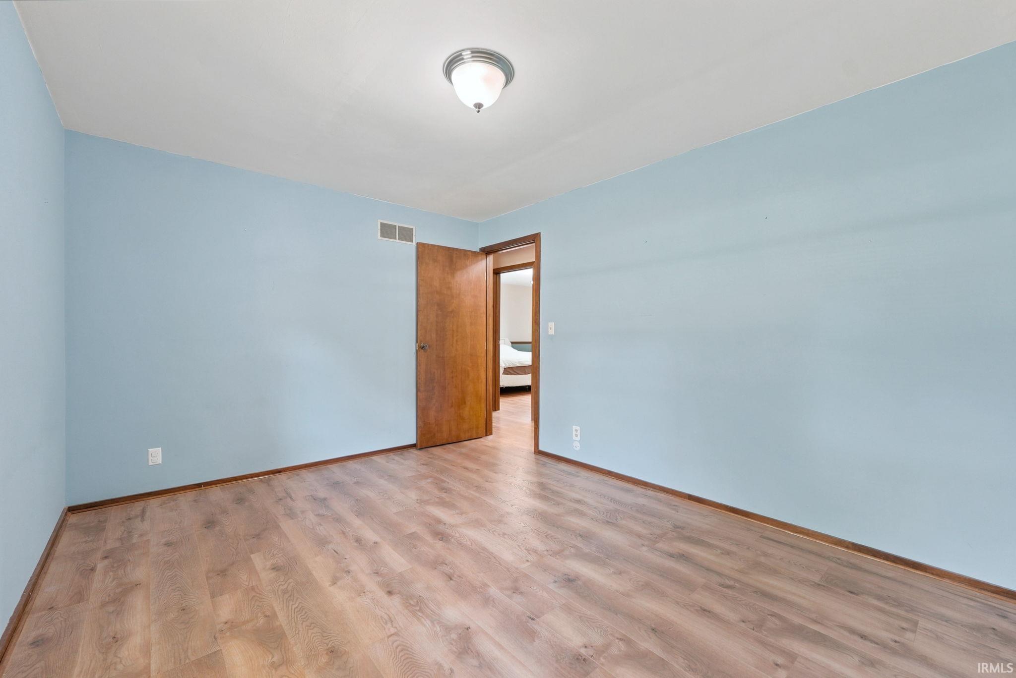 Room featuring wood-finish flooring, light blue wall paint, a ceiling-mounted light fixture, and a solid wood interior door