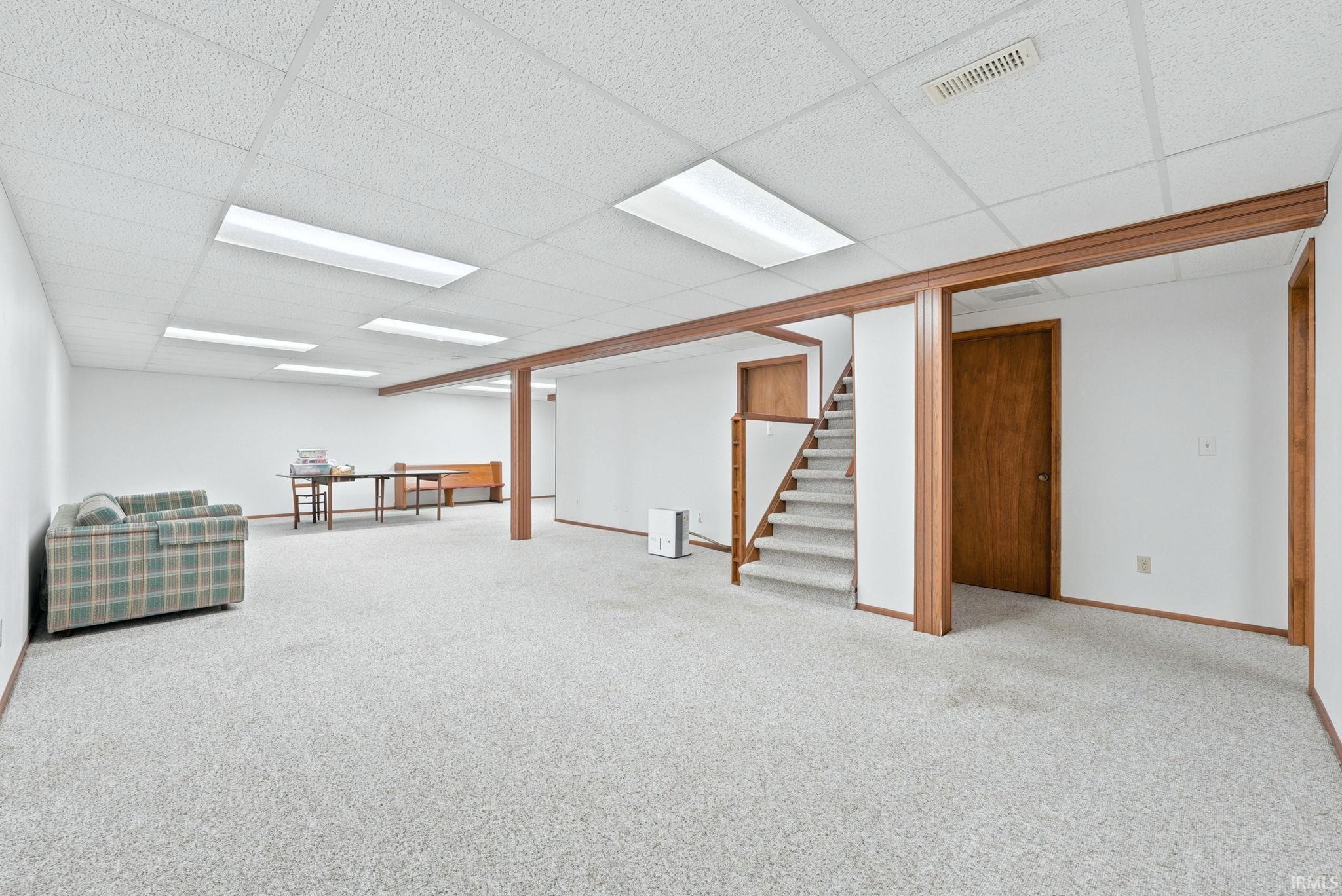 Spacious finished basement featuring light-toned carpeting, white walls, and a drop ceiling with integrated lighting