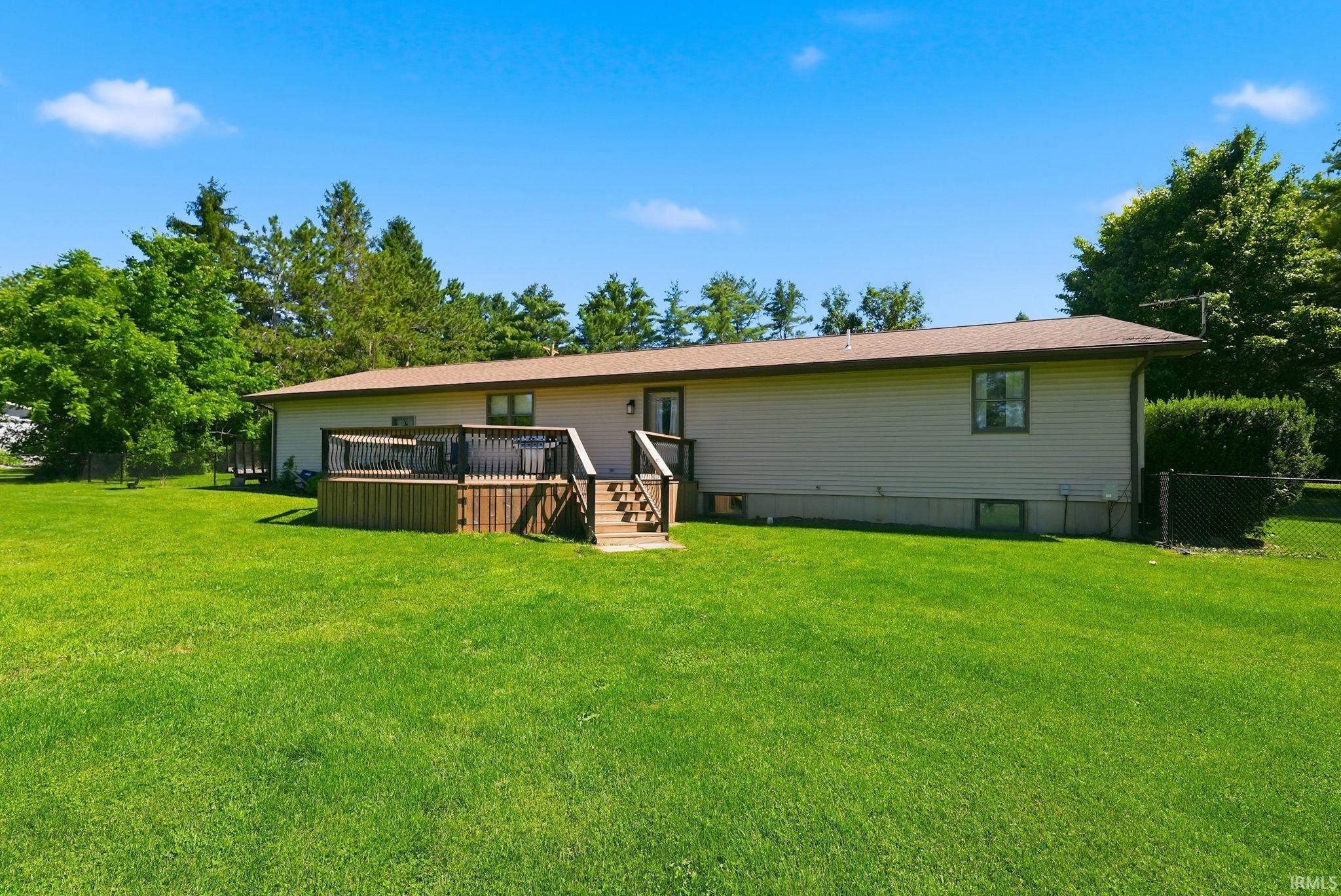 Expansive green lawn surrounds a property featuring light beige siding, a brown shingle roof, and a multi-level wood deck with steps