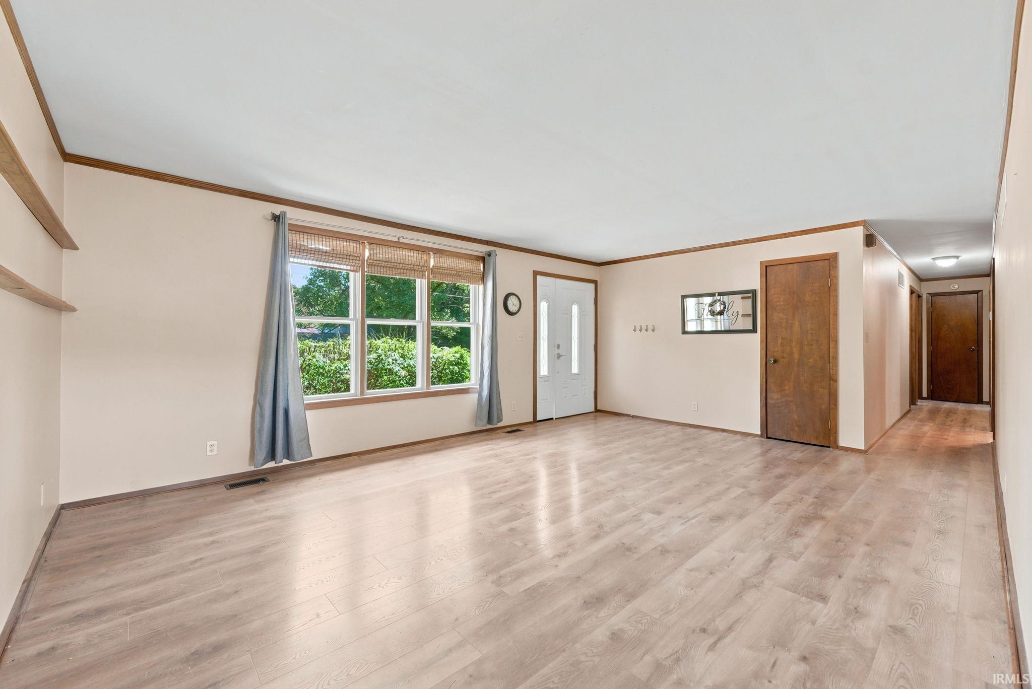 Spacious interior featuring wood-finish flooring, a large window, and light-toned walls with wood trim