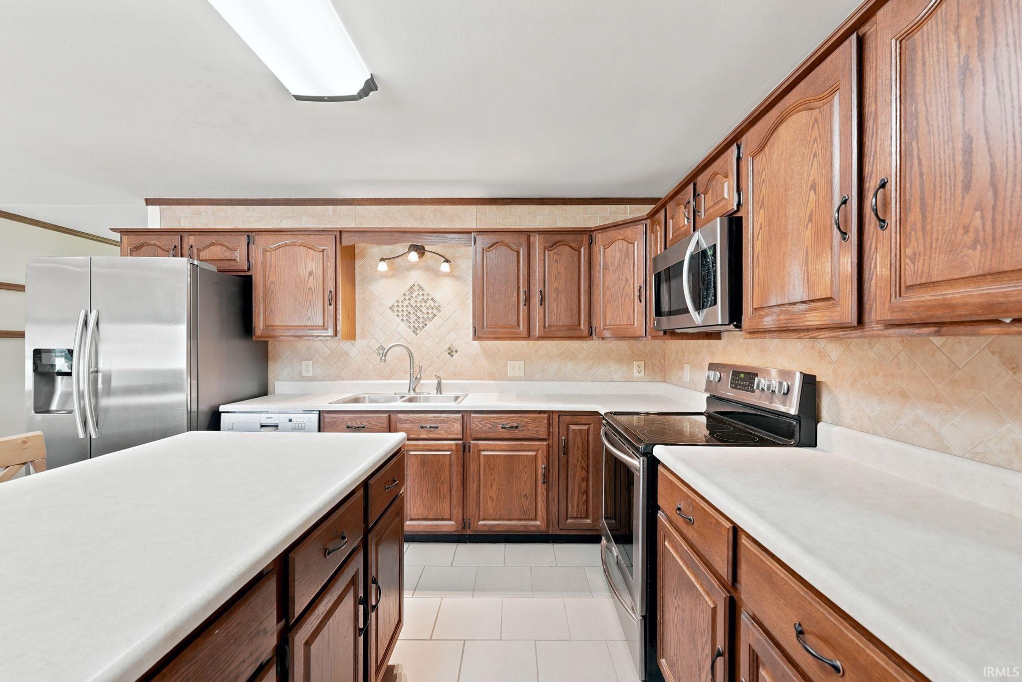 Kitchen featuring wood cabinetry, white countertops, tile flooring, and a patterned tile backsplash
