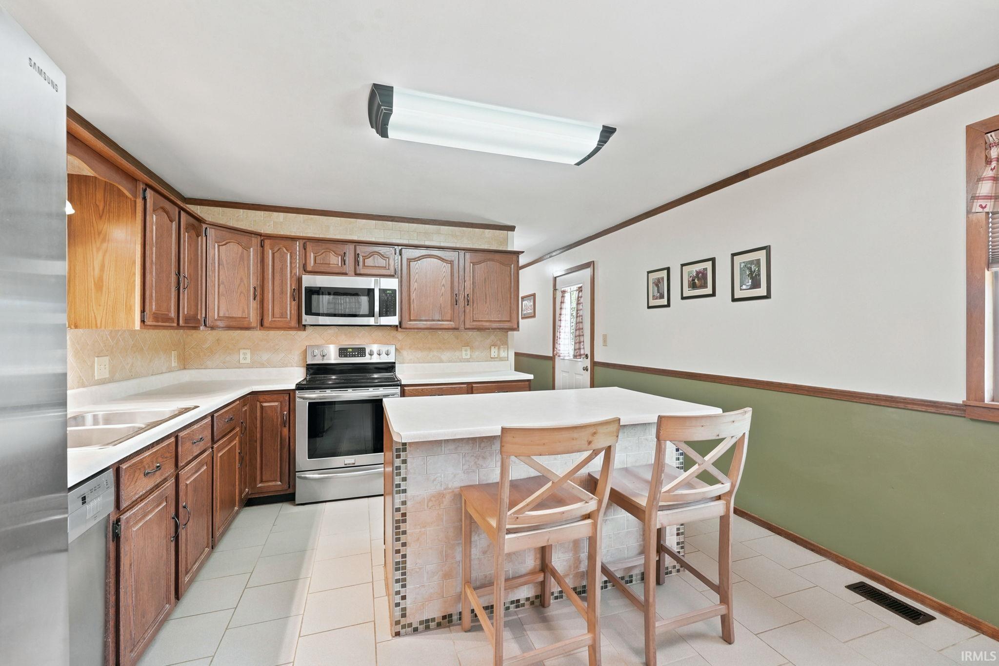 Kitchen featuring wood cabinetry, stainless steel appliances, a center island with bar seating, light-toned countertops, and tile flooring