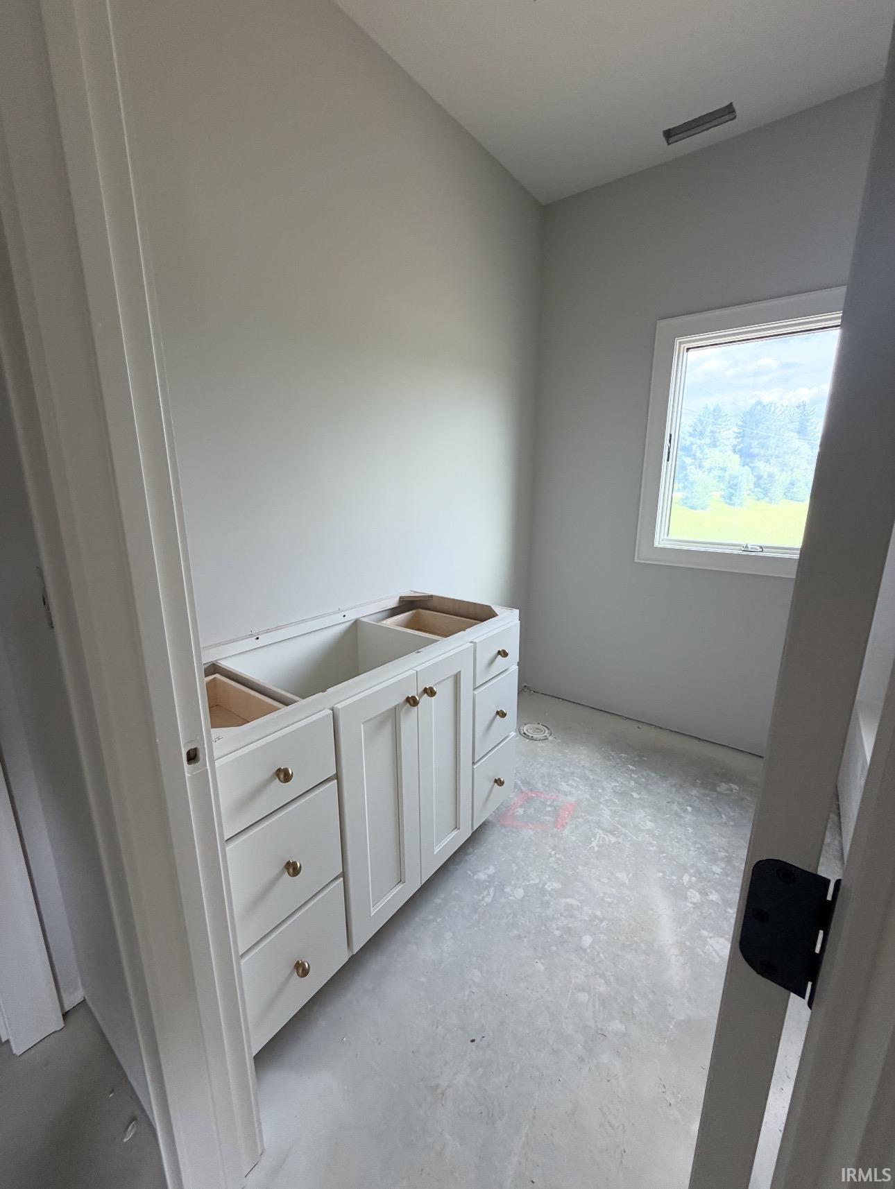 White shaker-style vanity with multiple drawers and cabinet doors, gold-toned hardware, and a single window