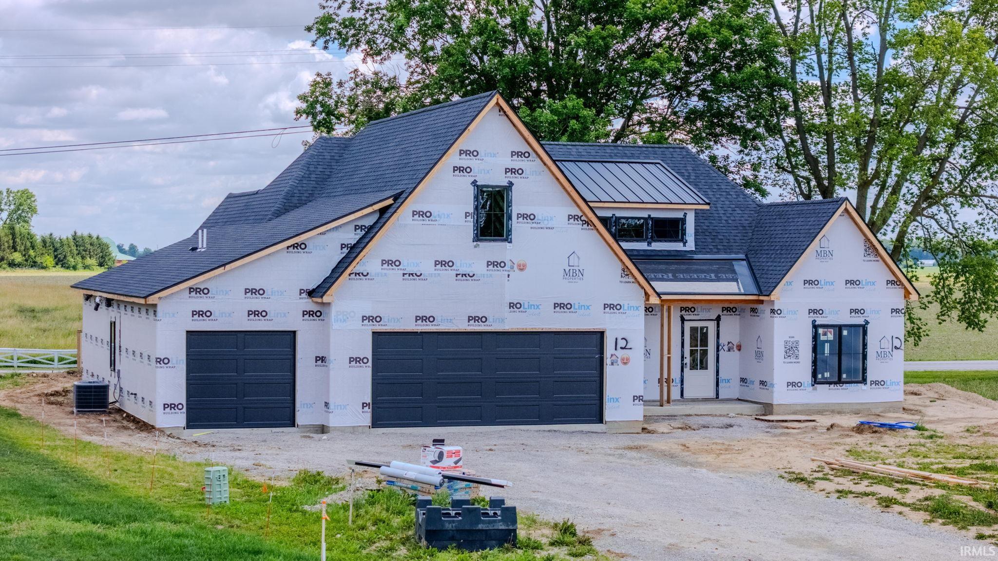 Newly constructed residence featuring a two-car garage, partial metal roof accent, and a gravel driveway