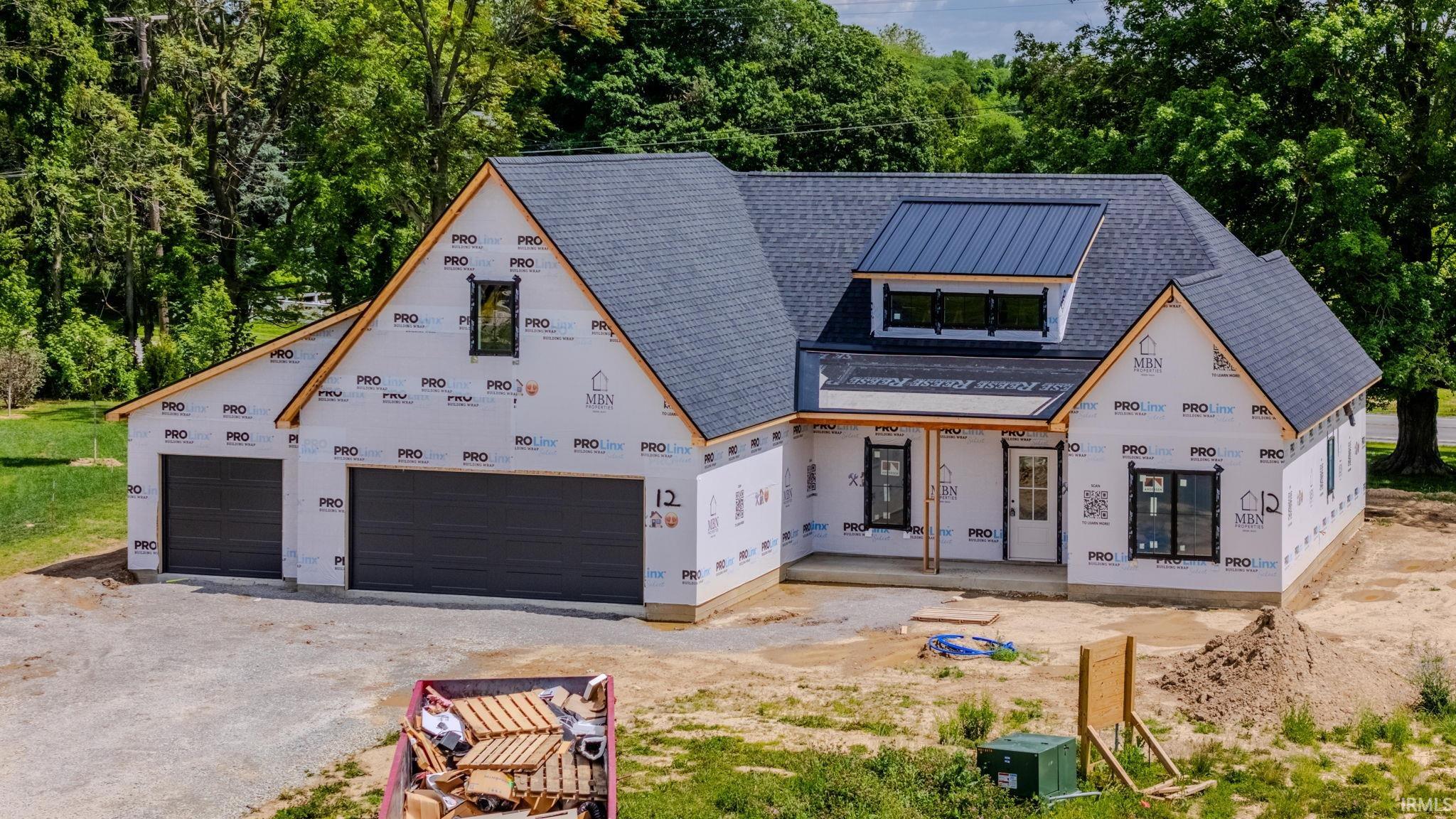 New construction residence featuring a dark shingle roof, integrated metal roof accent, two-car garage with dark paneled doors, black-framed windows, and a covered front porch