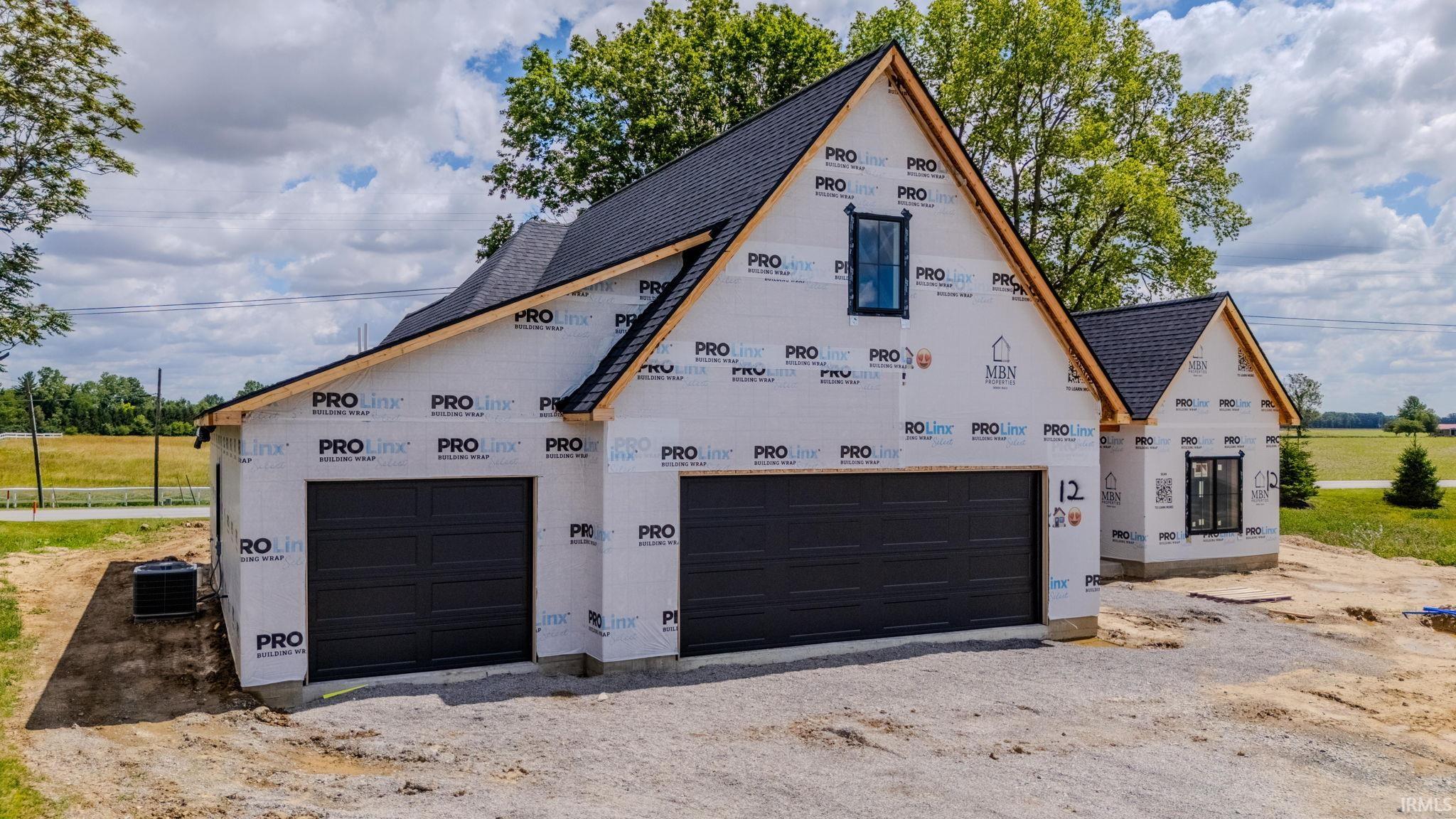 New construction featuring a multi-car garage with dark paneled doors and a black shingle roof