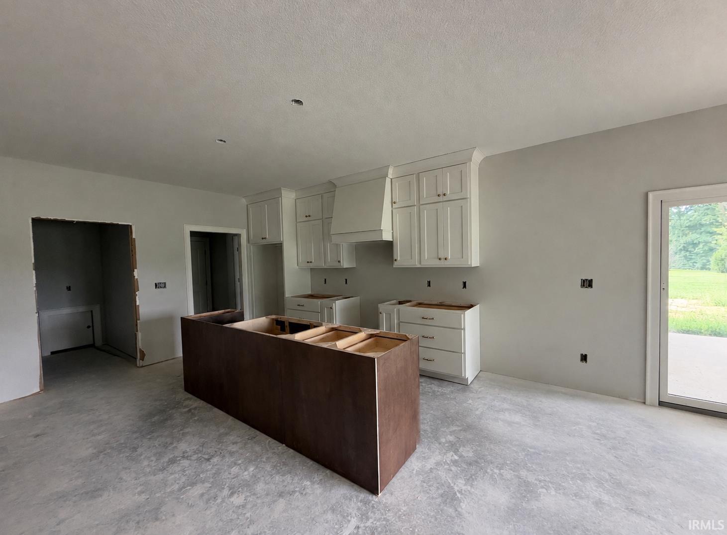 White shaker-style cabinetry with crown molding, central island with dark wood-finish base, ample wall space, and a glass-paneled exterior door