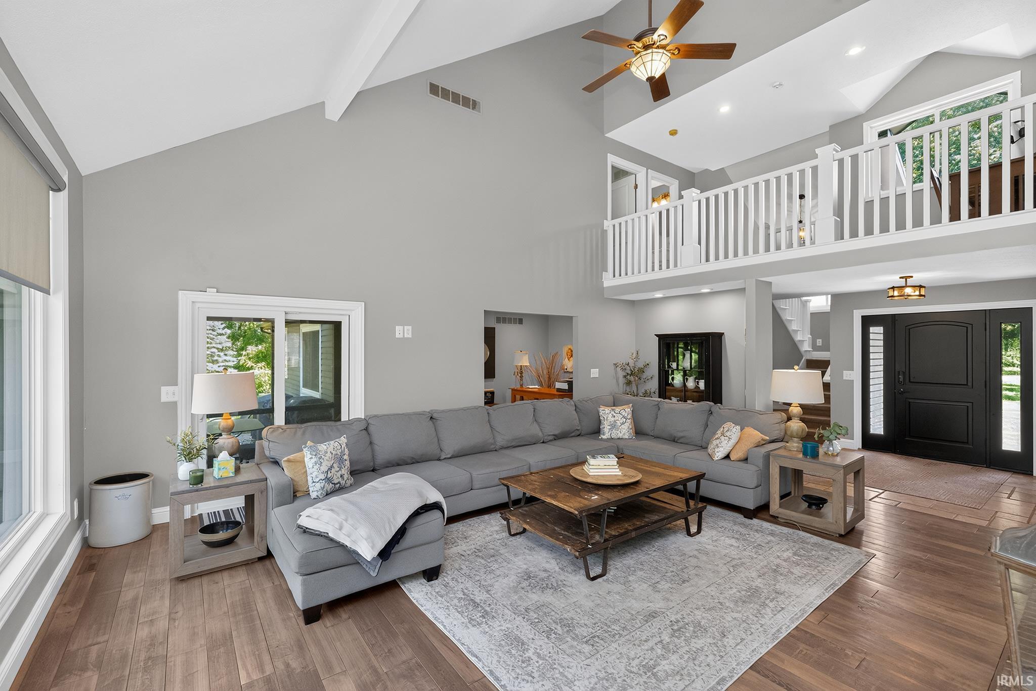 Vaulted ceiling great room featuring wood-finish flooring, a contemporary ceiling fan, and a second-story interior balcony with white spindle railing