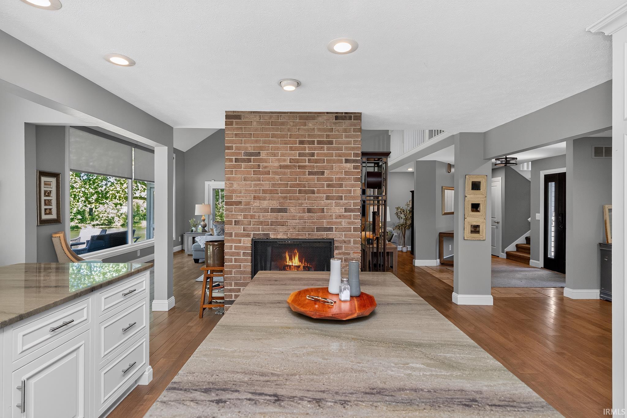 Kitchen island with a striated countertop, brick fireplace with a raised hearth, recessed lighting, hardwood flooring, and white cabinetry