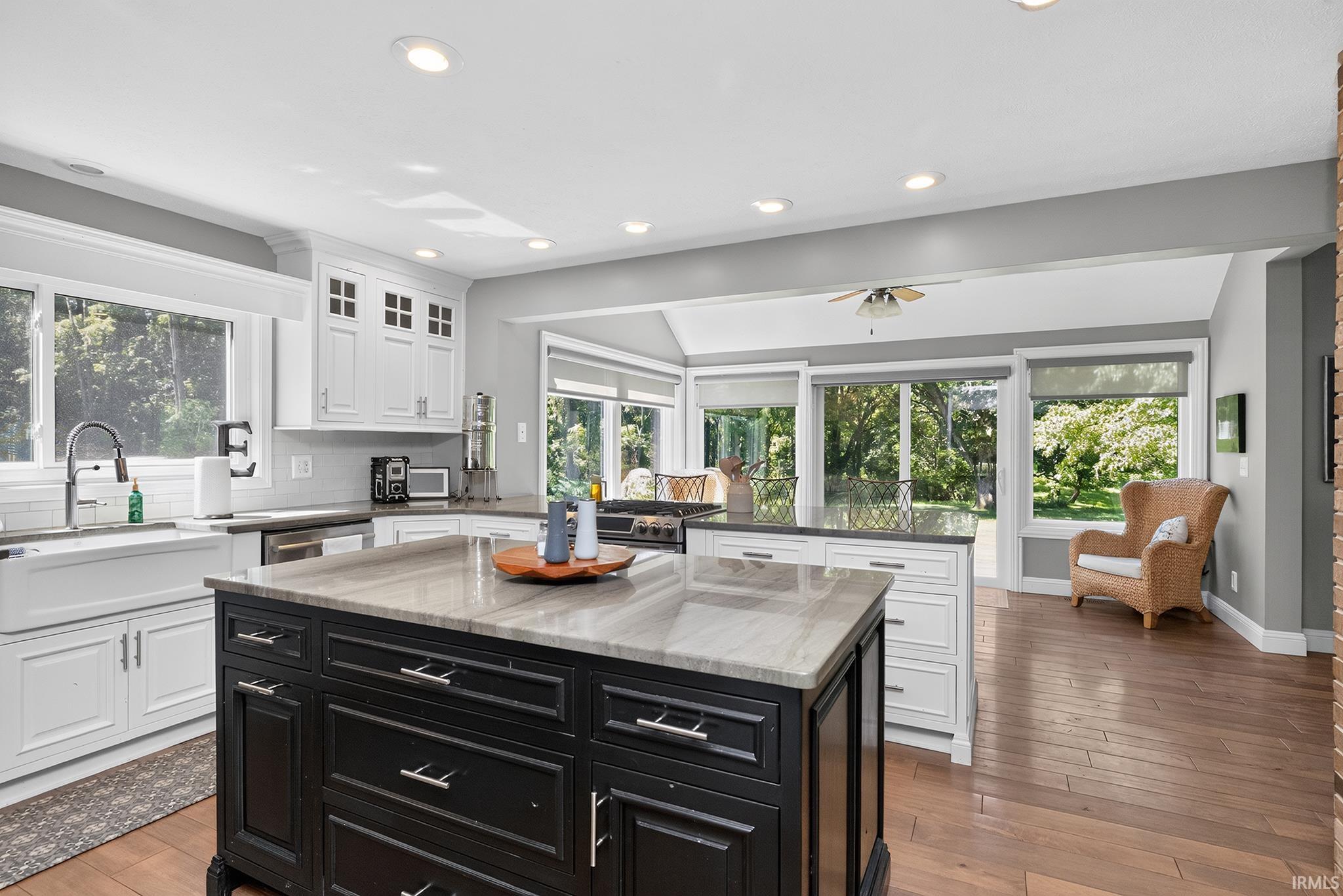 Kitchen featuring a two-tone island with stone countertop, white perimeter cabinetry, stainless steel appliances, and wood-finish flooring