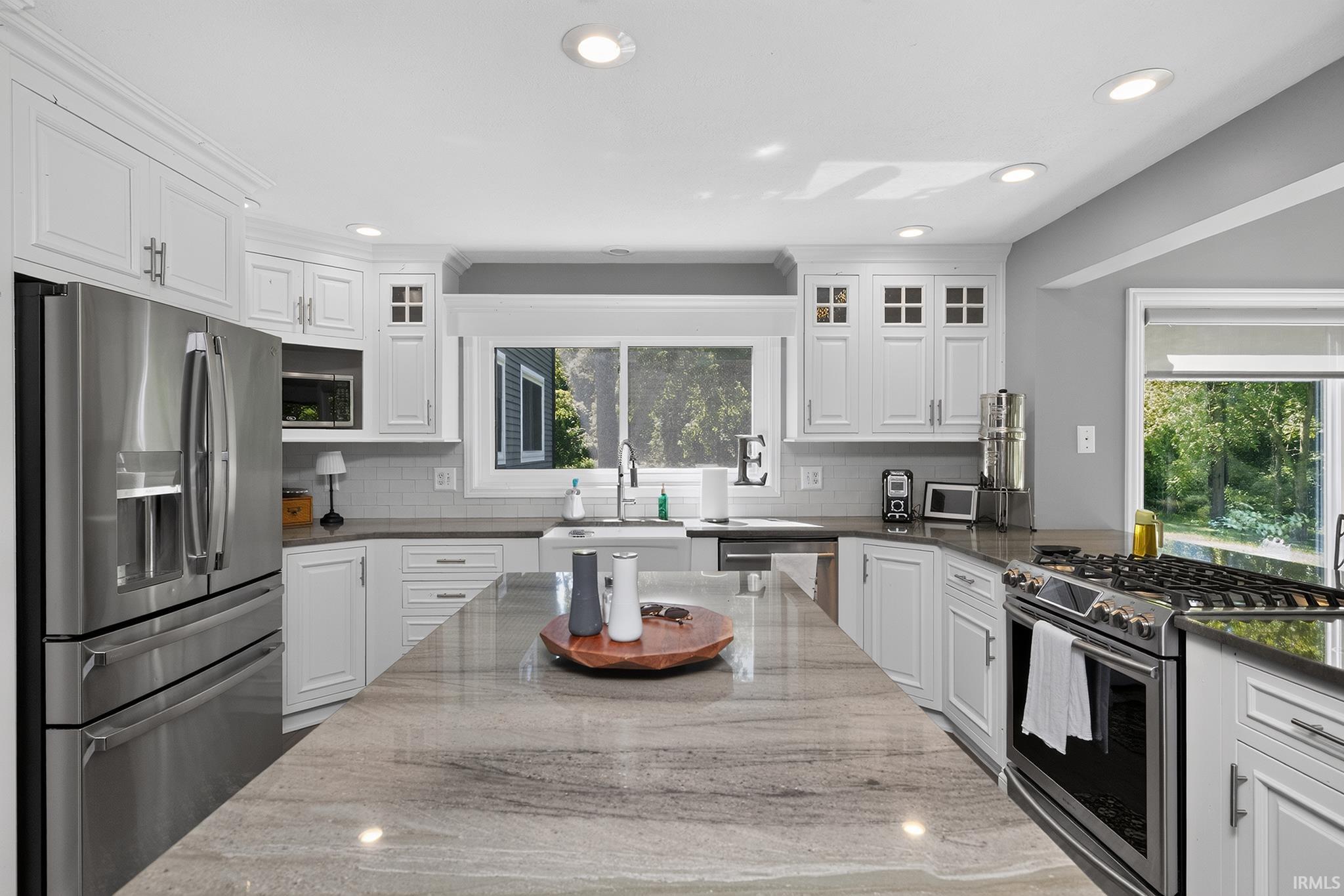 Kitchen featuring a large central island with a stone countertop, white cabinetry with crown molding, stainless steel appliances, and recessed lighting