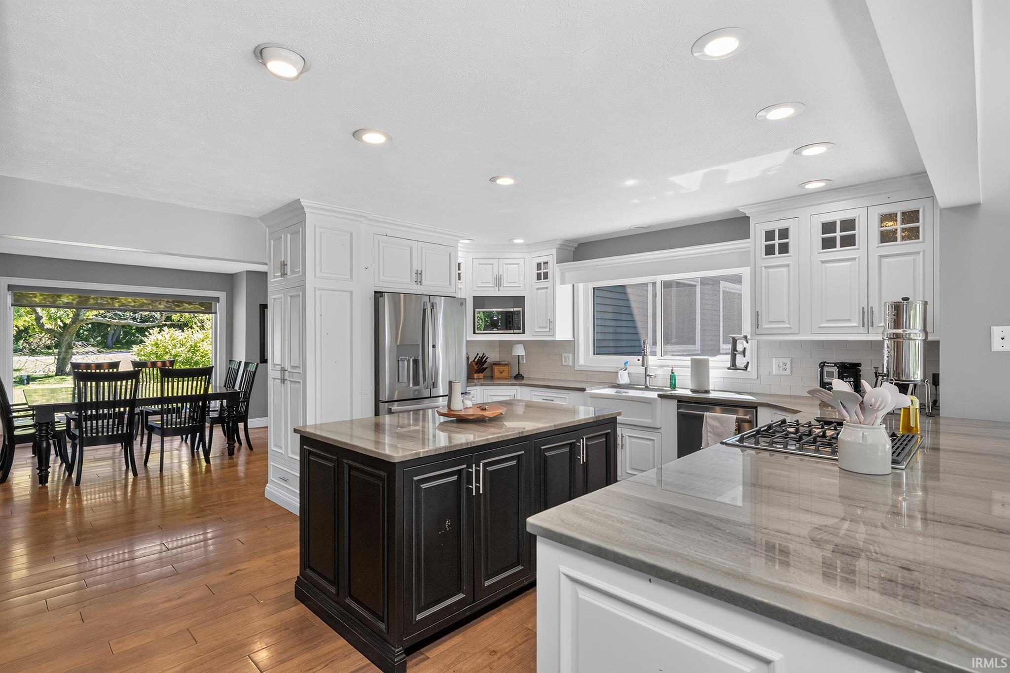 Modern kitchen featuring white shaker cabinetry, stainless steel appliances, a center island with dark wood-finish cabinetry, light-toned stone countertops, and wood-finish flooring