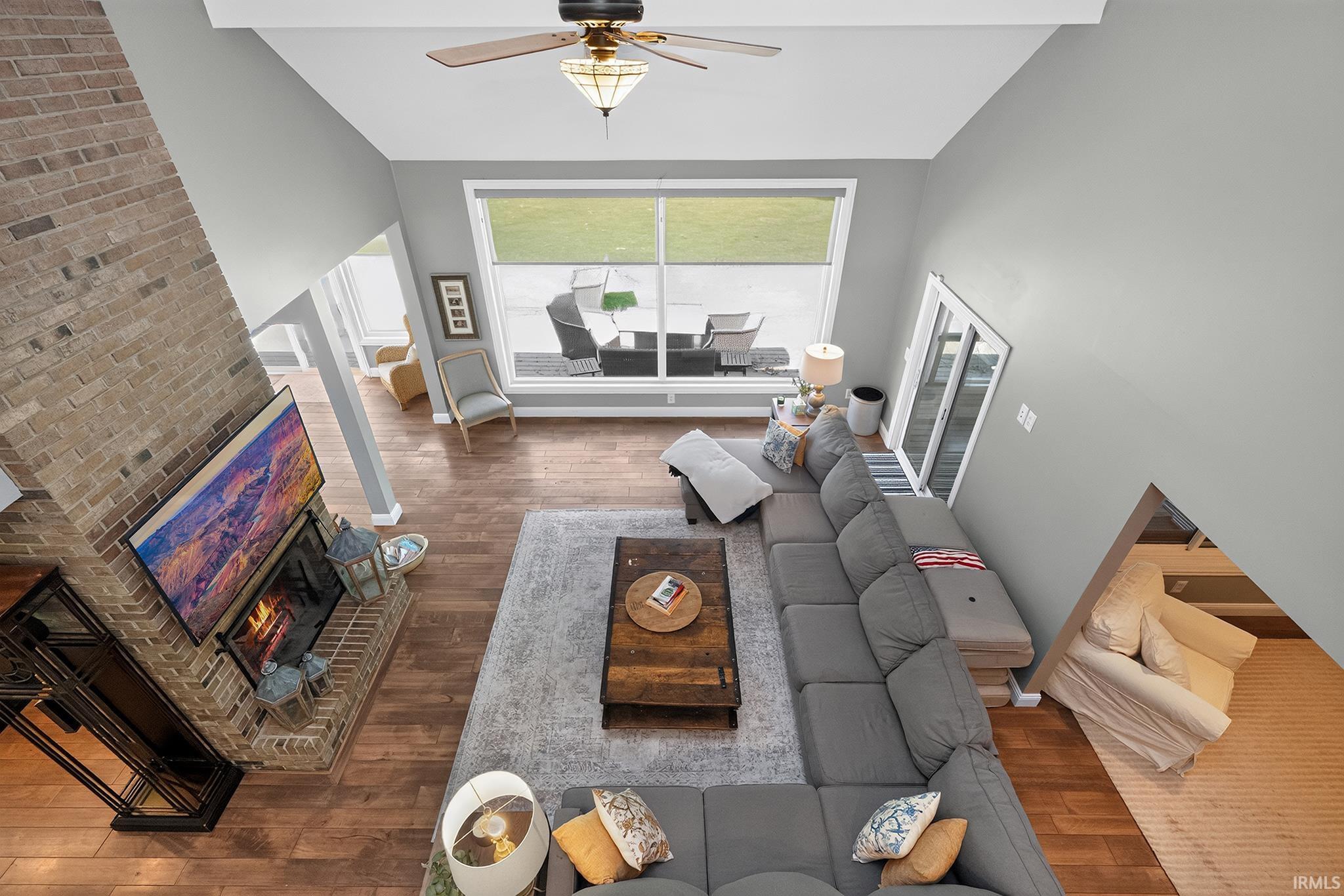Great room featuring a prominent brick fireplace with a built-in mantel, wood-finish flooring, and vaulted ceilings with a ceiling fan